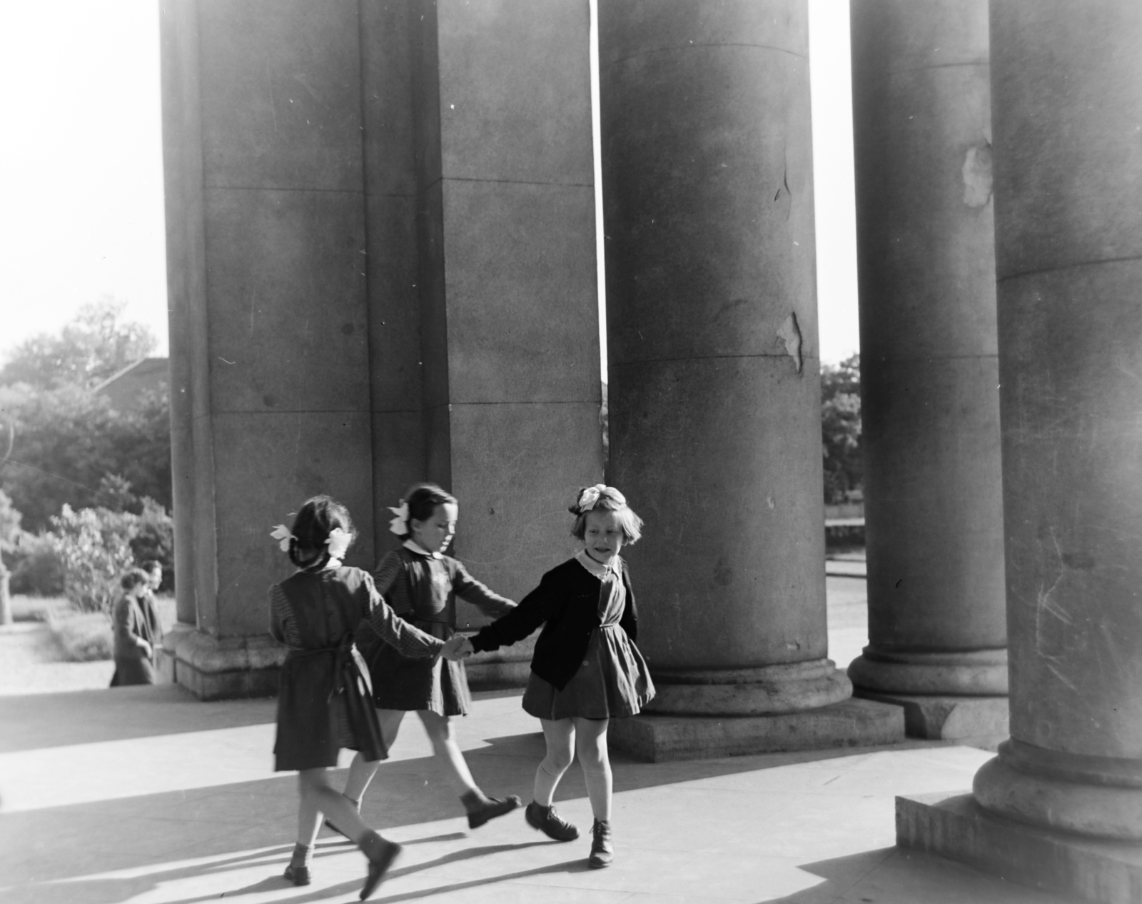 Magyarország, Budapest VIII., Magyarok Nagyasszonya (Rezső) tér, a felvétel a Magyarok Nagyasszonya-templom kapujánál készült., 1957, Keveházi János, Budapest, lányok, masni, oszlop, tánc, Fortepan #197502