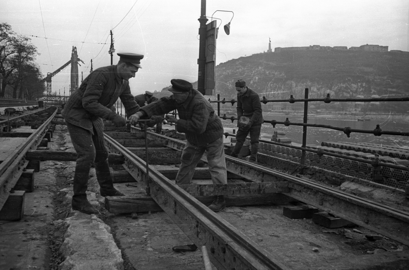 Hungary, Budapest V., Dunakorzó, a villamospálya javítása. Háttérben a lerombolt Erzsébet híd pesti hídfője és a Gellért-hegy., 1956, Bauer Sándor, Budapest, soldier, rails, worker, sleeper, peaked cap, Fortepan #199449