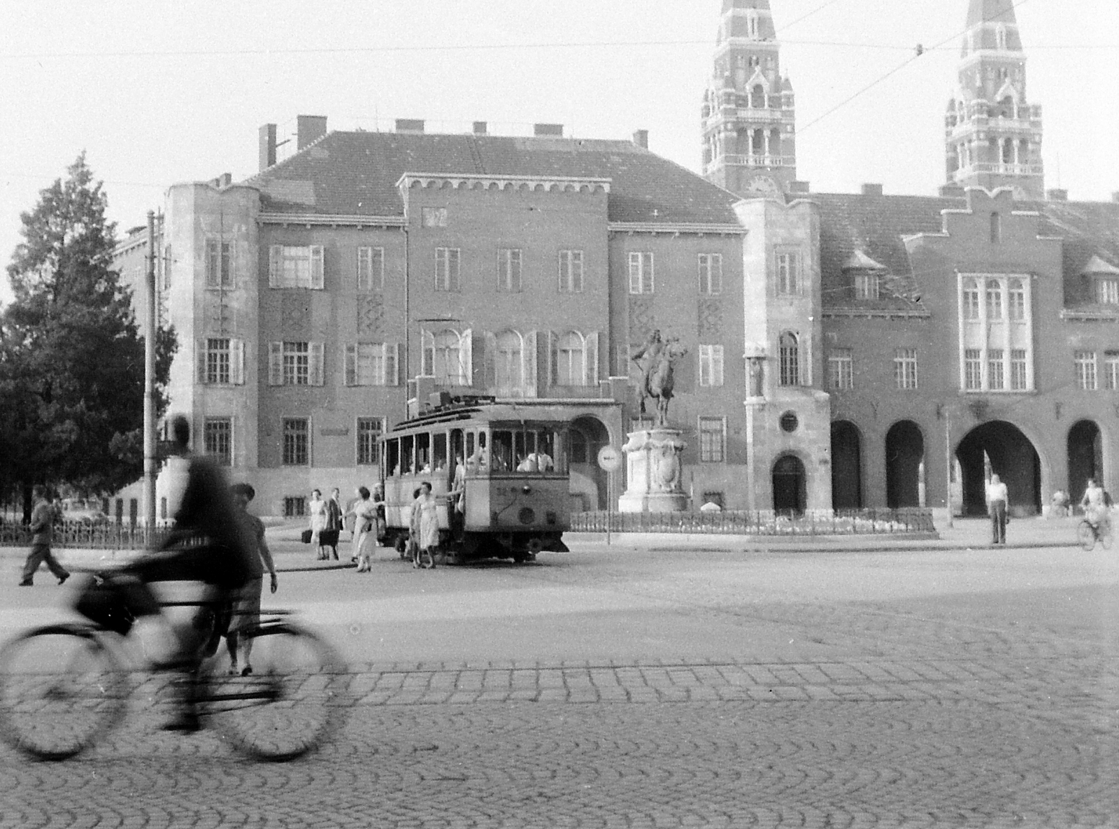 Magyarország, Szeged, Aradi vértanúk tere. Az egyetem épületei mögött a Fogadalmi templom tornyai., 1955, Gyöngyi, kerékpár, kapu, villamos, kockakő, neogótika, lovas szobor, II. Rákóczi Ferenc-ábrázolás, Fortepan #1998