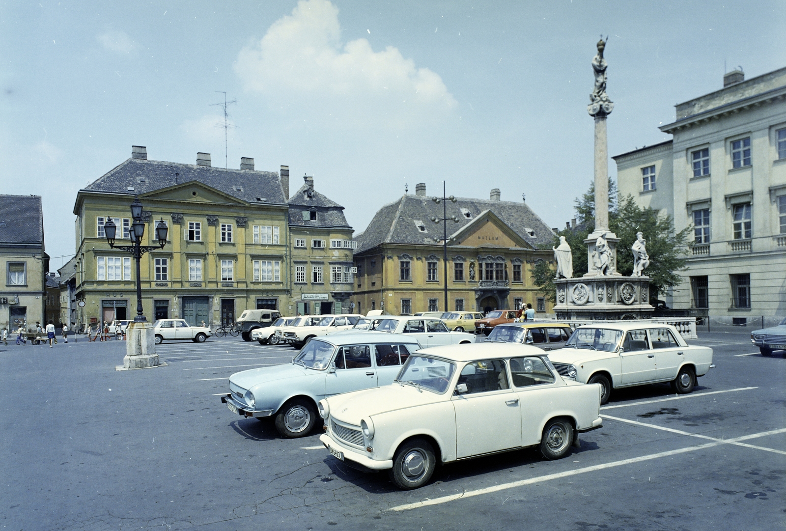 Magyarország, Győr, Széchenyi tér, balra a Kenyér köz torkolata. Középen a Stelczer Lajos utca sarkán a Vastuskós ház és a Xantus János Múzeum (Apátúr ház). Előtérben a Mária oszlop Buda 1686. évi visszafoglalásának emlékére, mögötte a Rába Városi Művelődési Központ (egykori Lloyd székház, ma irodaház)., 1976, FŐFOTÓ, színes, parkoló, Fortepan #207039