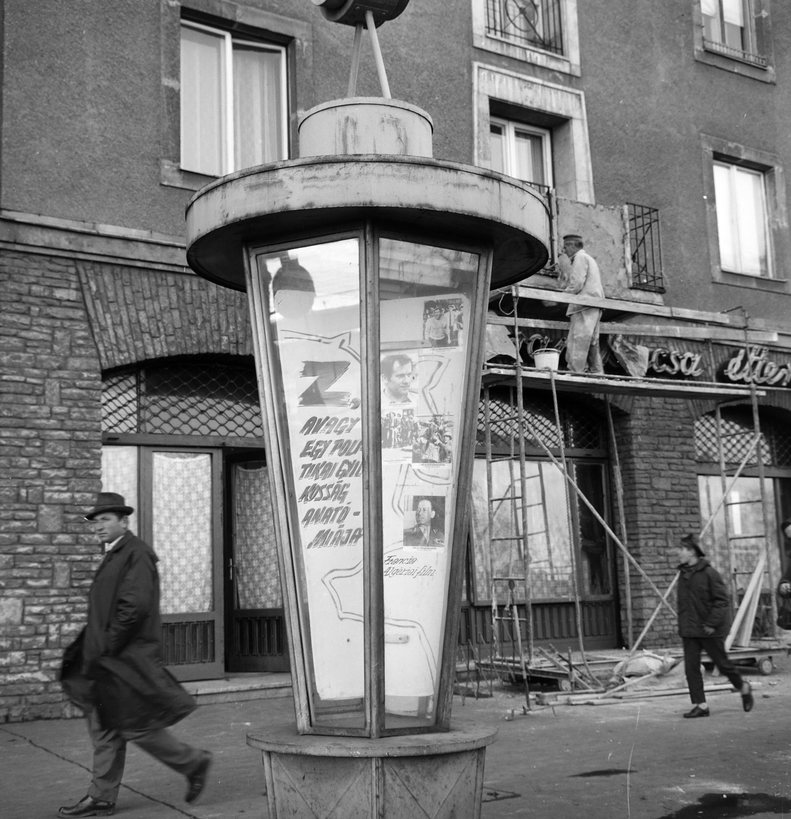 Magyarország, Budapest XIV., az Örs vezér tere 2-es számú ház előtt a Fővárosi Moziüzemi Vállalat (FŐMO) által forgalmazott filmeket hirdető vitrinoszlop. Háttérben az erkély helyreállítása látható, miután a műmárvány térplasztikát, súllya és a balesetveszély miatt eltávolították., 1969, FŐFOTÓ, Budapest, Fortepan #208136