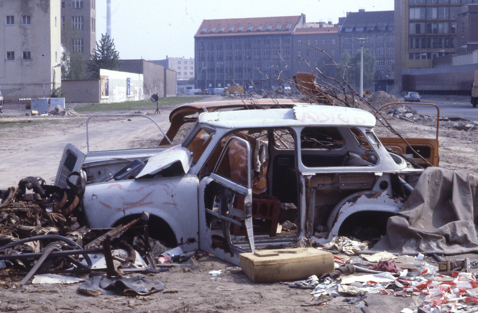 Németország, Berlin, a berlini fal egykori biztonsági zónája a Schützenstraße (balra) és a Zimmerstraße (jobbra) között az Alex-Springer-Straße (Lindenstraße) felé nézve, jobb szélen az Axel Springer toronyház alsó szintjei látszanak., 1990, Urbán Tamás, Trabant-márka, színes, járműroncs, Fortepan #213683