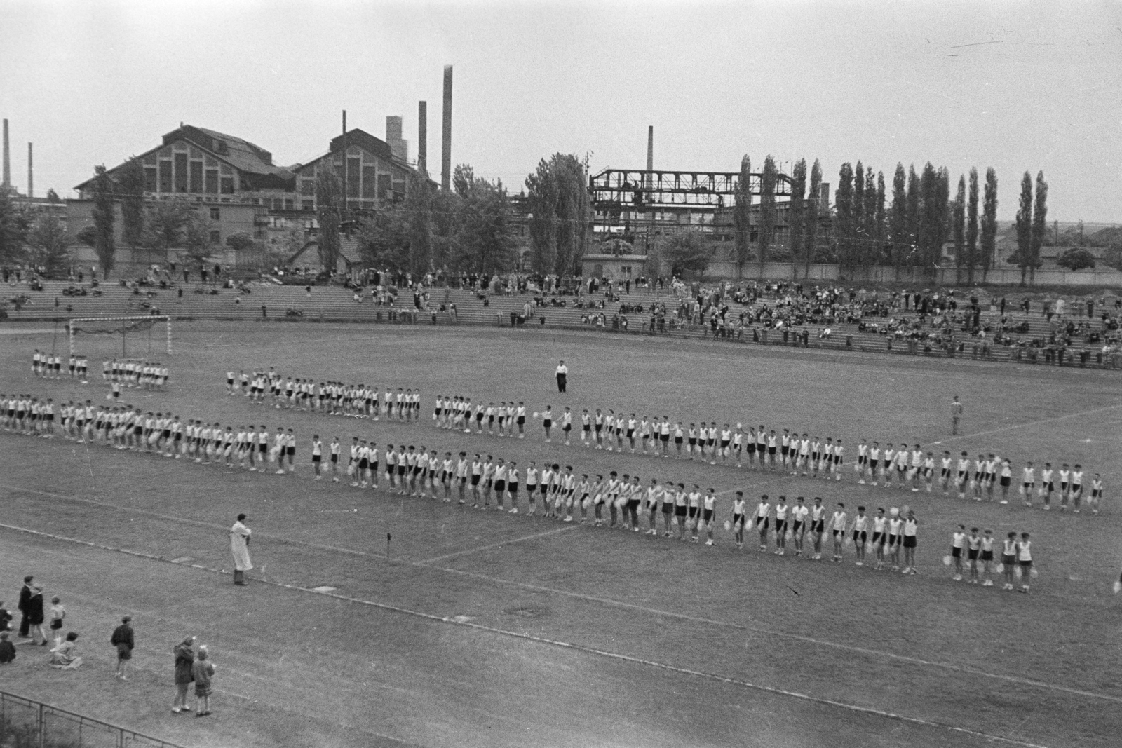 Magyarország, Budapest XIX.,Budapest XVIII., a Budapesti Honvéd SE pályája, tornebemutató, háttérben a Lőrinci Hengermű., 1954, Várkonyi Andrea, Budapest, közönség, hengermű, torna, fiúk, sportpálya, Fortepan #213945