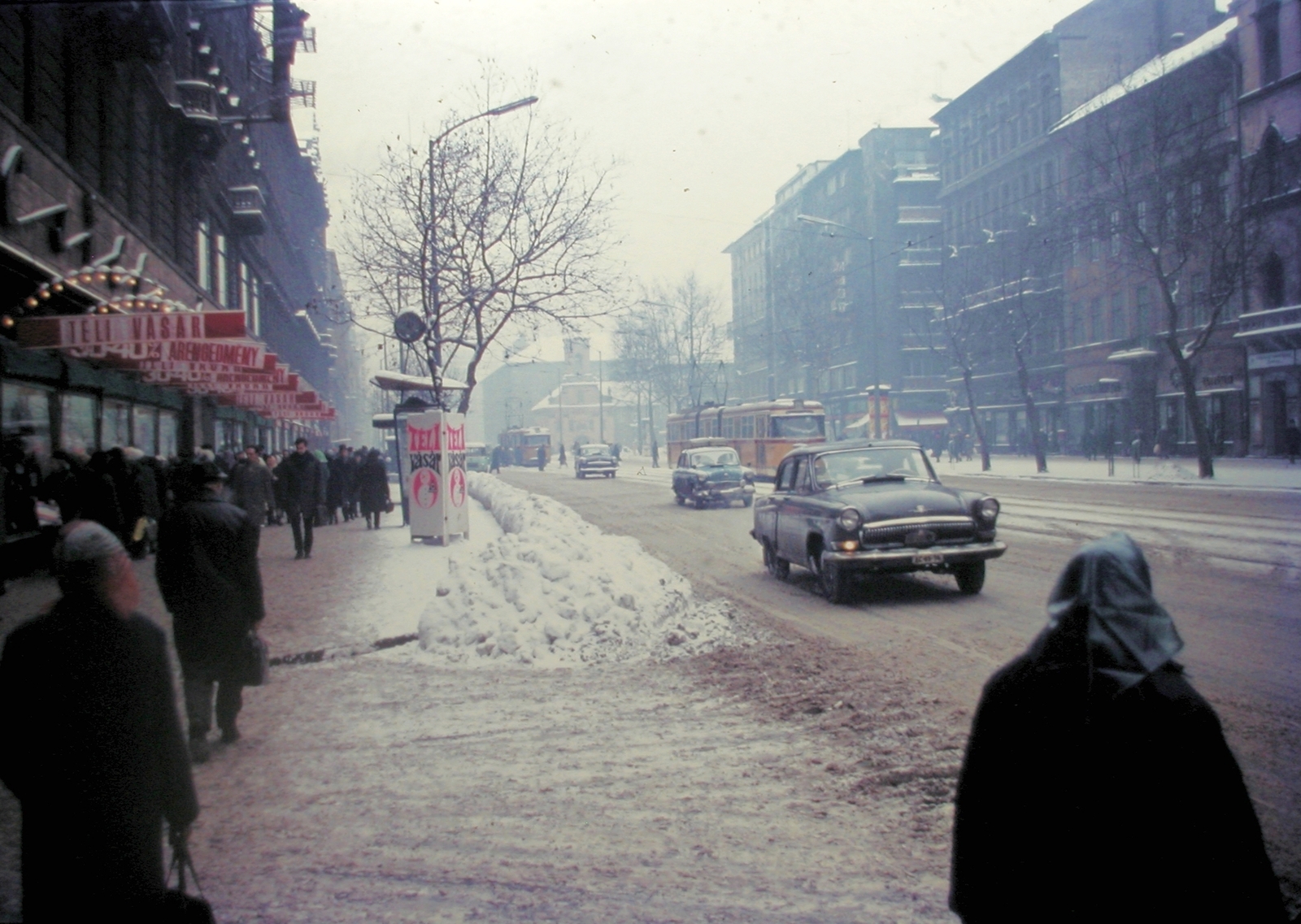 Magyarország, Budapest VII., Rákóczi út - Kazinczy utca sarok, szemben a Szent Rókus kápolna., 1970, Fortepan, tél, hó, színes, villamos, áruház, GAZ M21 Volga, FVV CSM-2/CSM-4, neon felirat, Budapest, Fortepan #21402