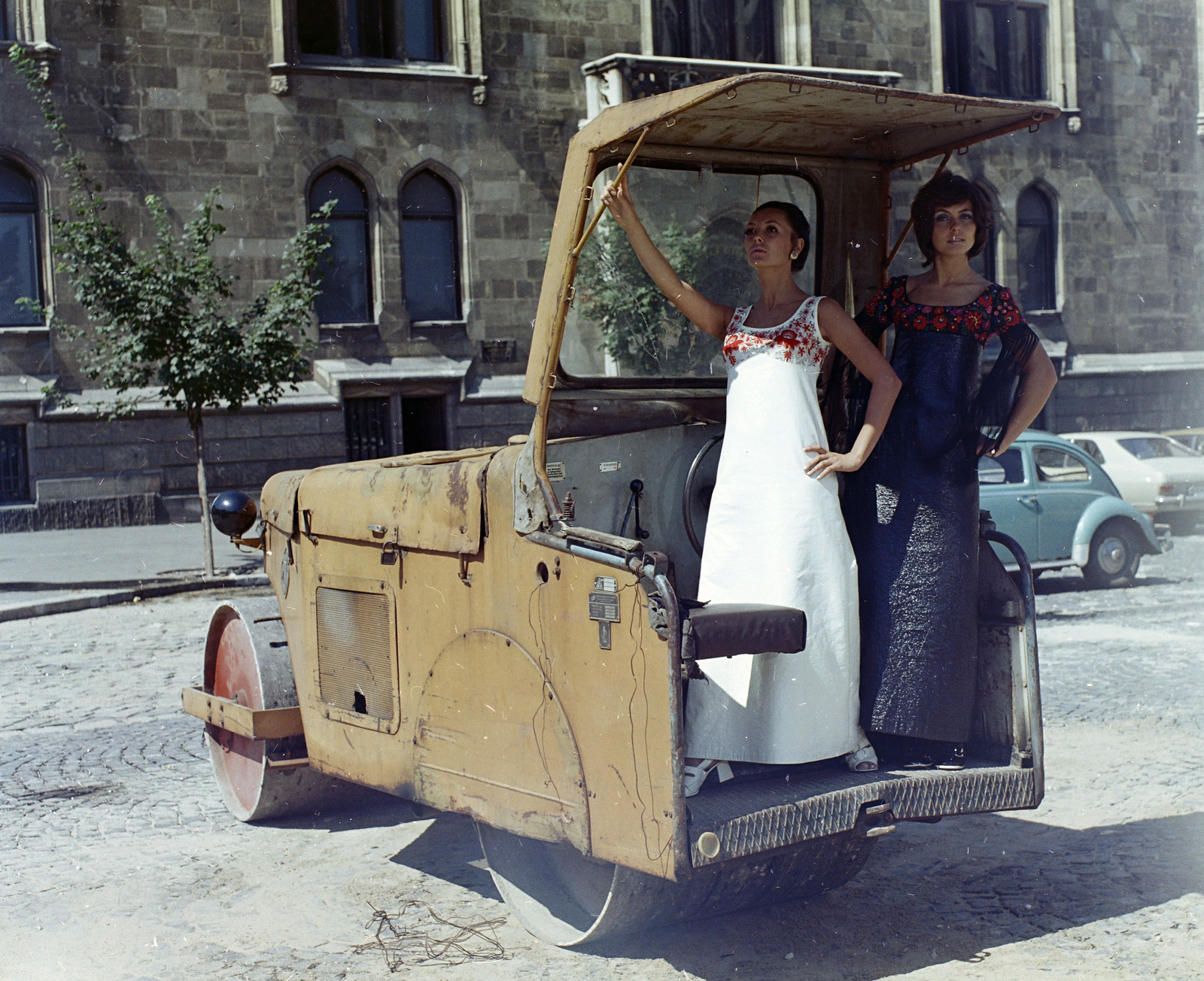 Hungary, Budapest I., Szentháromság tér, a felvétel a BME Schönherz Zoltán Kollégiuma (az egykori Pénzügyminisztérium épülete) előtt készült. Takács Zsuzsa és Szilágyi Mari manökenek., 1970, FŐFOTÓ, fashion, women, road roller, Budapest, dress, Matyó folk costume, embroidery, fashion photo, girls'n'cars, Fortepan #214874