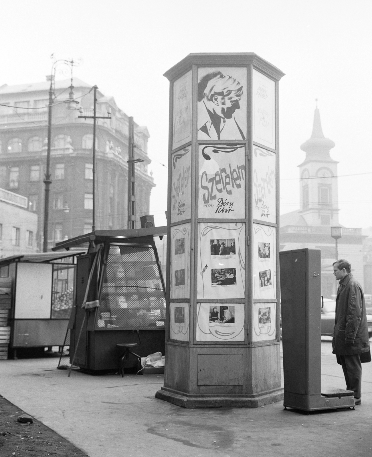 Magyarország, Budapest VIII.,Budapest IX., Kálvin tér a Múzeum utca és a Baross utca közötti tűzfal előtt. A Fővárosi Moziüzemi Vállalat (FŐMO) által forgalmazott film hirdetése mögött, balra az Állami Biztosító központi épülete, jobbra a református templom., 1971, FŐFOTÓ, Budapest, férfi, hirdetőoszlop, bódé, mérleg, Fortepan #215224