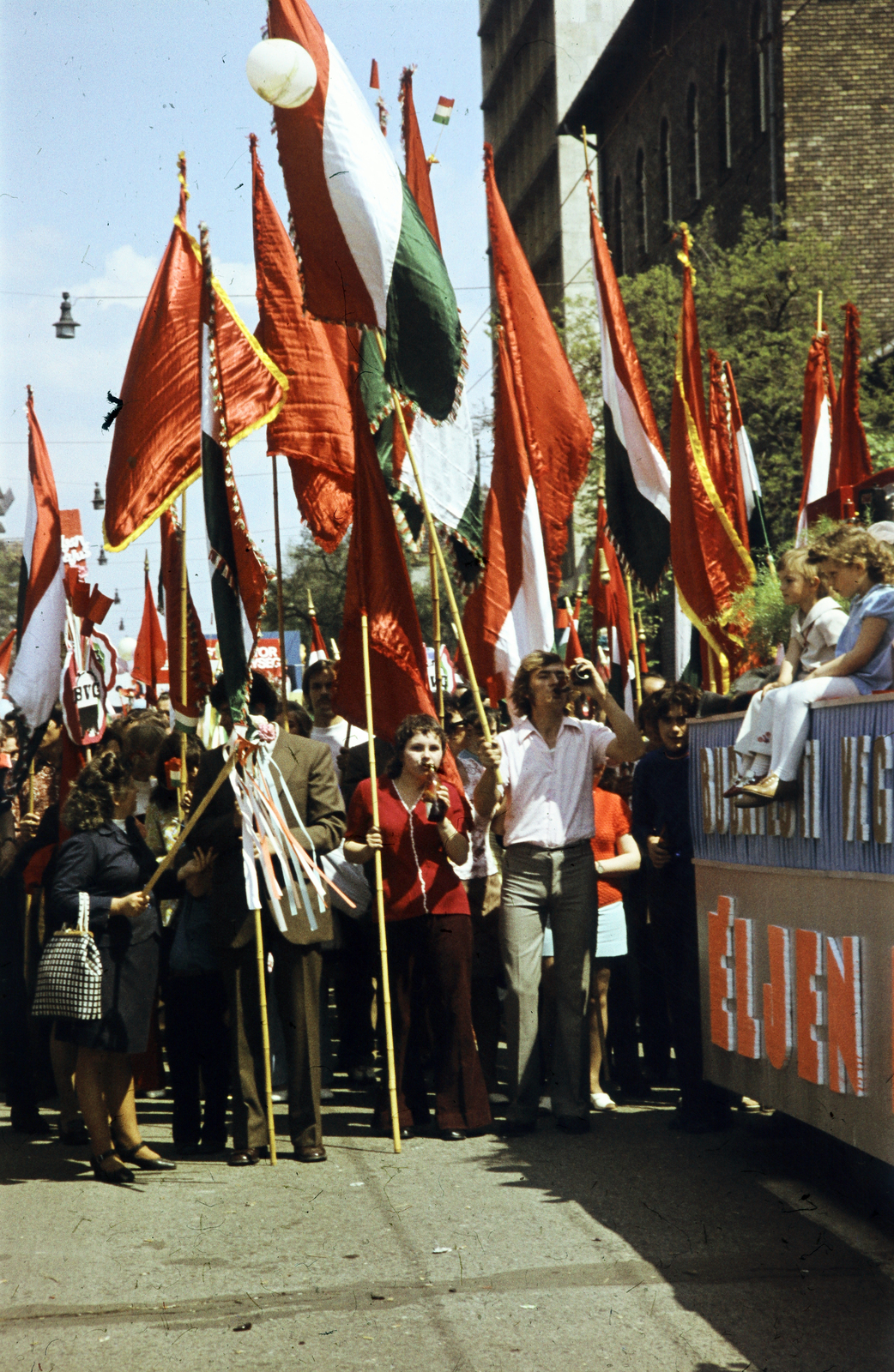 Magyarország, Budapest XIV., Ajtósi Dürer sor, május 1-i felvonulás résztvevői, jobbra a Zichy Géza utca sarkán álló épület látható., 1970, Benedek Tamás, színes, felvonulás, május 1, zászló, pódiumautó, Budapest, Fortepan #218391