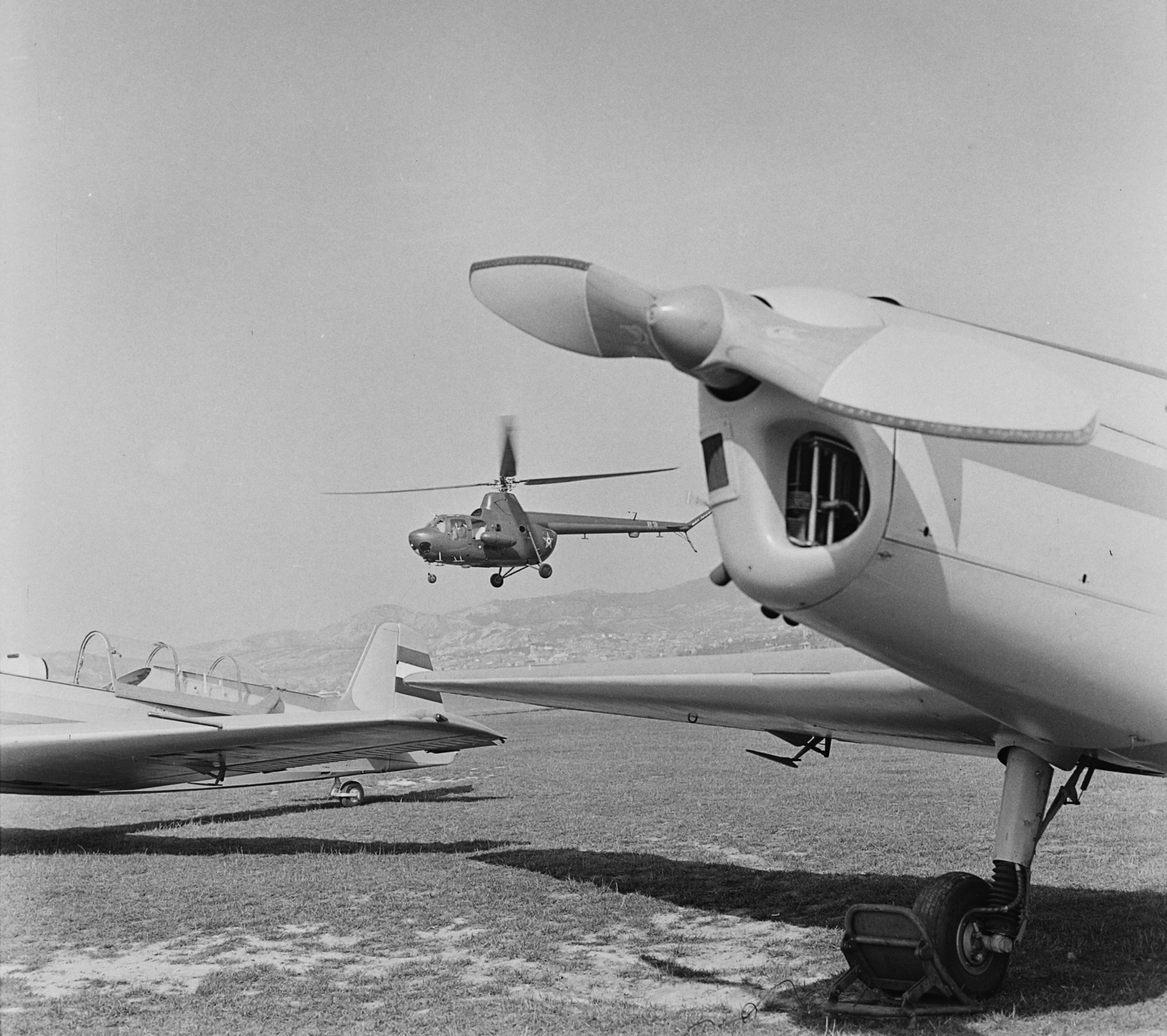 Magyarország, Budaörsi repülőtér, Budapest XI., Zlin Trener repülőgép az előtérben, a háttérben egy Mi-1 típusú katonai helikopter., 1968, MHSZ, közlekedés, csehszlovák gyártmány, szovjet gyártmány, repülőgép, katonaság, helikopter, repülőtér, Zlin-márka, légcsavar, Mil-márka, Mil Mi-1, Zlin Z-226, Budapest, Fortepan #22153
