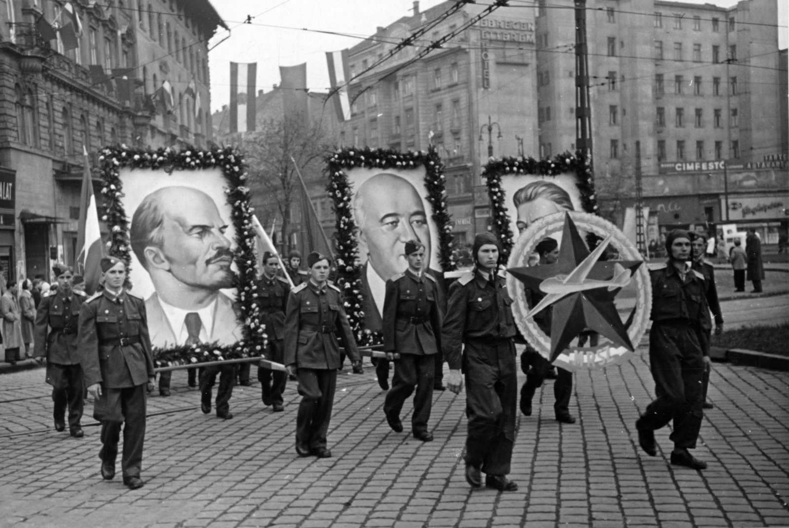 Hungary, Budapest VIII.,Budapest VII., Baross tér, szemben a Rákóczi út. Repülősök a május 1-i felvonuláson., 1953, Nasztanovics Ferenc, sign painter, Budapest, hold in arms, uniform, Red Star, Lenin-portrayal, march, Joseph Stalin portrayal, Mátyás Rákosi-portrayal, flower decoration, flying, Hungarian Defense Association, Fortepan #222178