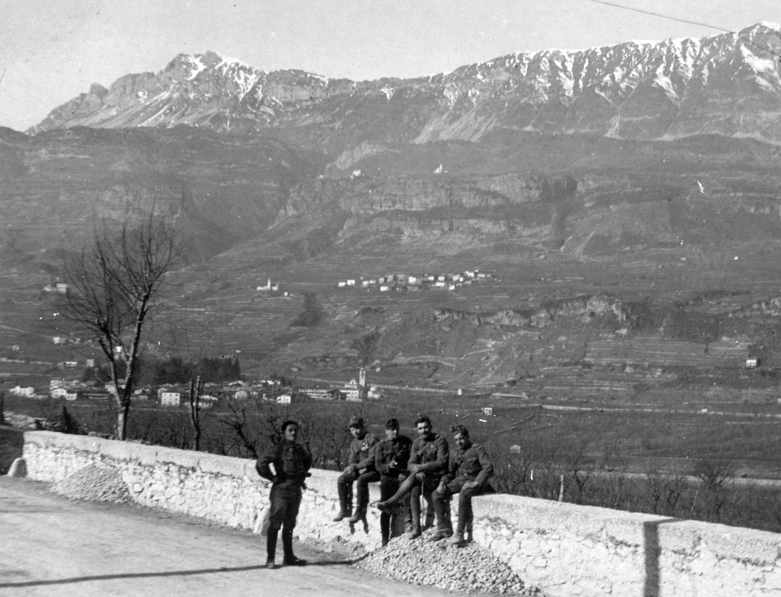 Olaszország, Volano, alul középen a Chiesa della Purificazione templom, a völgy túloldalán Pedersano község, a háttérben a Monte Stivo sziklás csúcsa látszik., 1916, Vogl Elemér, első világháború, falu, templom, egyenruha, csoportkép, férfiak, völgy, hegy, falon ülni, Fortepan #23901