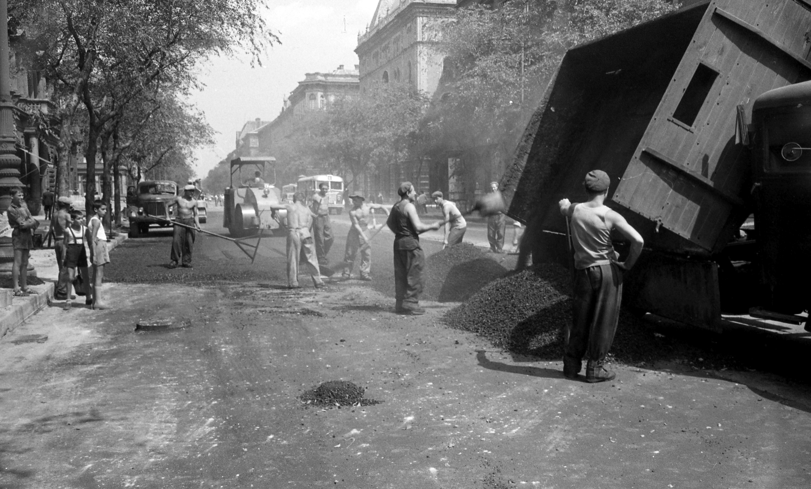 Magyarország, Budapest VI., Andrássy út (Népköztársaság útja), a túloldalon középen a Drechsler-palota a Dalszínház utca és a Hajós utca között. A felvétel az Andrássy út (Népköztársaság útja) Bajcsy-Zsilinszky út és az Oktogon (November 7. tér) közötti szakaszának 1960. nyarán történt átépítése során készült., 1960, FŐMTERV, Domonkos Endre, Budapest, rövidnadrág, fiúk, munkás, kíváncsiság, útépítés, aszfaltozás, úthenger, Fortepan #251353