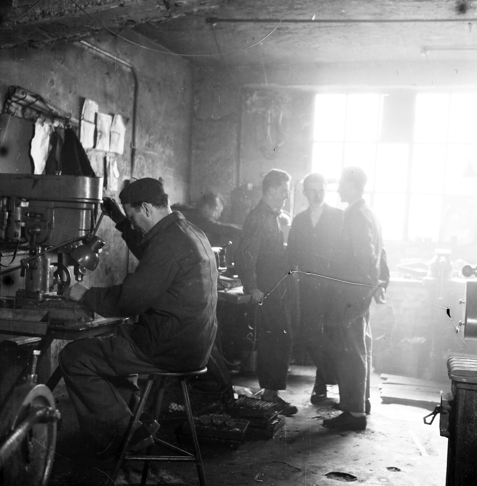 Magyarország, Budapest XIII., Kassák Lajos utca (Fóti út) 13., Lakatos- és Fémáru Kisipari Termelő Szövetkezet. FO-32 oszlopos fúrógépen dolgozó szakmunkás, mögötte ipari tanulók., 1958, Ungváry Rudolf, Budapest, műhely, ellenfény, állványos fúró, Fortepan #254863