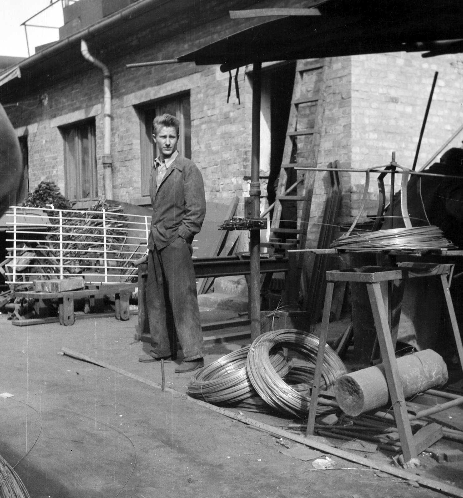 Magyarország, Budapest XIII., Kassák Lajos utca (Fóti út) 13., Lakatos- és Fémáru Kisipari Termelő Szövetkezet. Szakmunkás segéd az üzem udvarán, a lakatosműhely előtt., 1958, Ungváry Rudolf, Budapest, zsebredugott kéz, Fortepan #254912