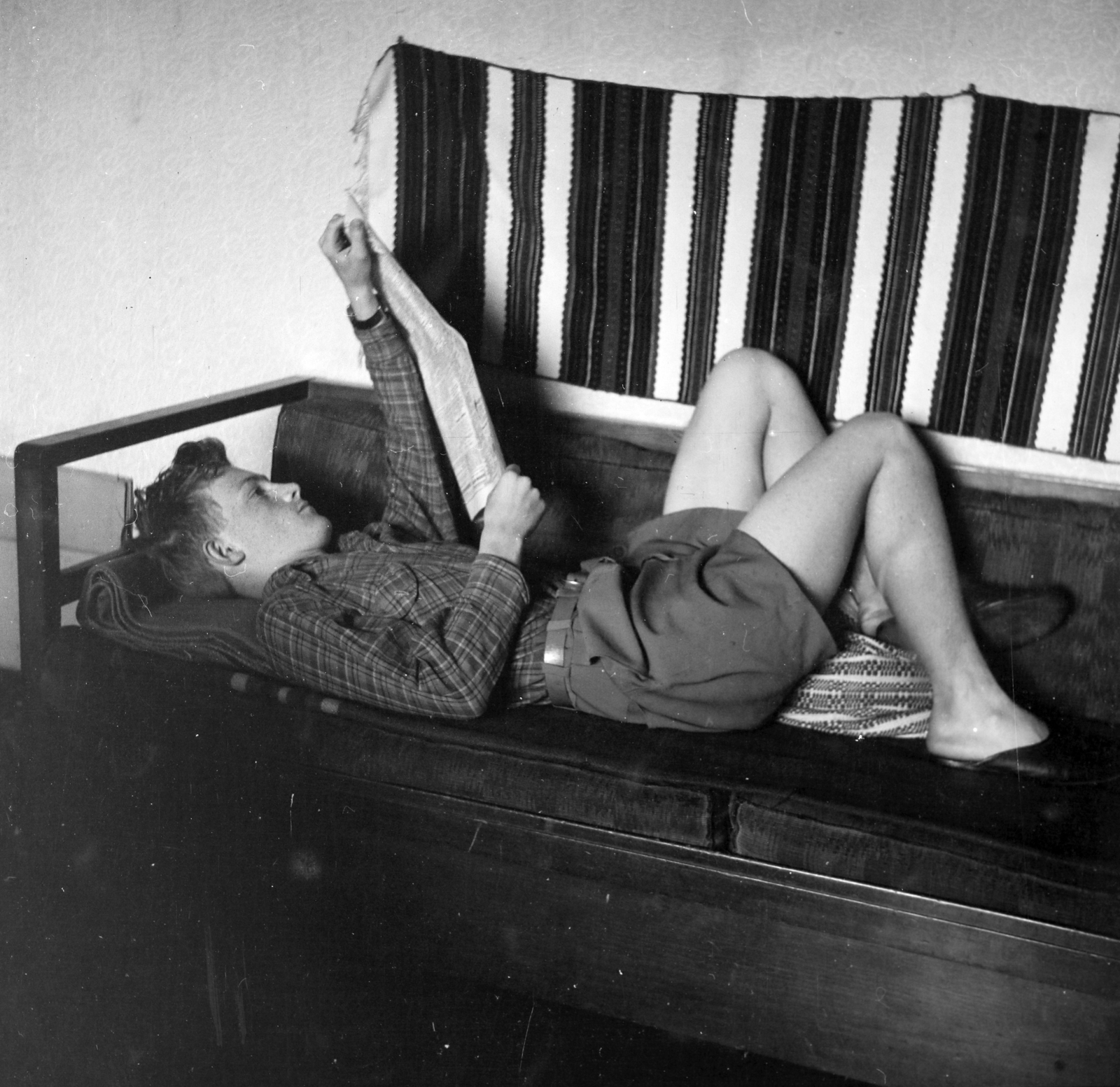 Magyarország, Budapest XIII., a felvétel a Bulcsú utca 21/a számú ház egyik lakásában készült., 1954, Ungváry Rudolf, Budapest, képarány: négyzetes, kamasz, szőttes, falvédő, papucs, rövidnadrág, olvasás, újság, kanapé, fiú, Best of, Fortepan #254989