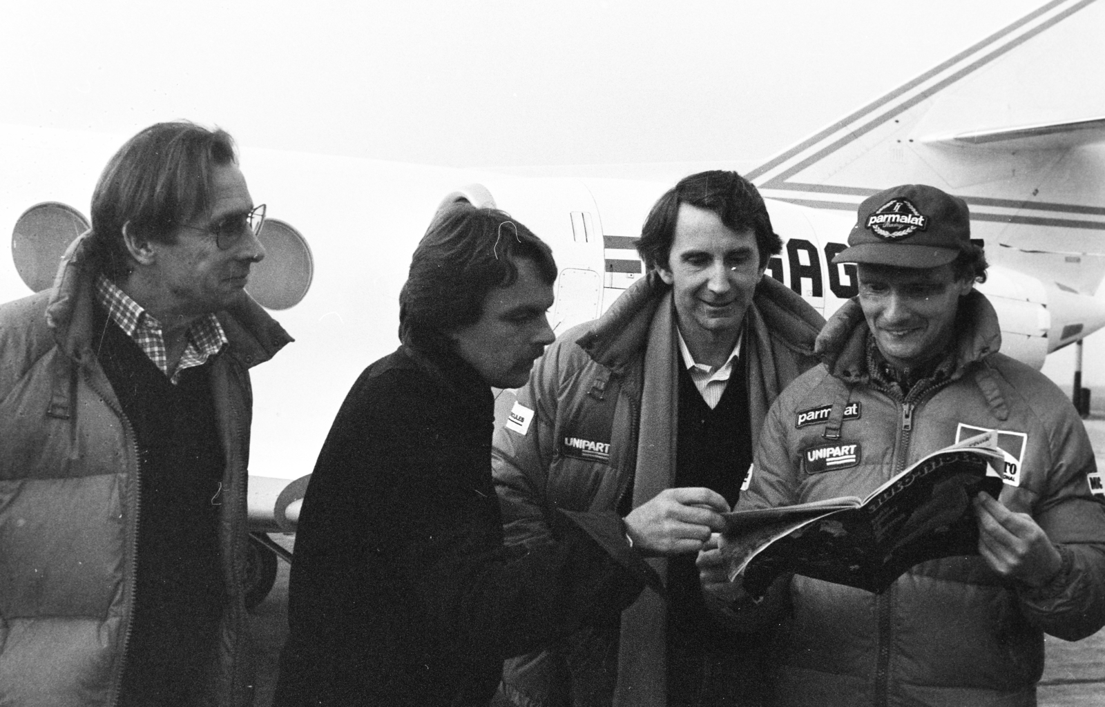 Magyarország, Ferihegyi (ma Liszt Ferenc) repülőtér, Budapest XVIII., balra a Marlboro-cég motorsport-részlegének vezetője, majd Keke Rosberg, John Watson és Niki Lauda., 1982, Bojár Sándor, Budapest, autóverseny, híres ember, olvasás, Fortepan #255361