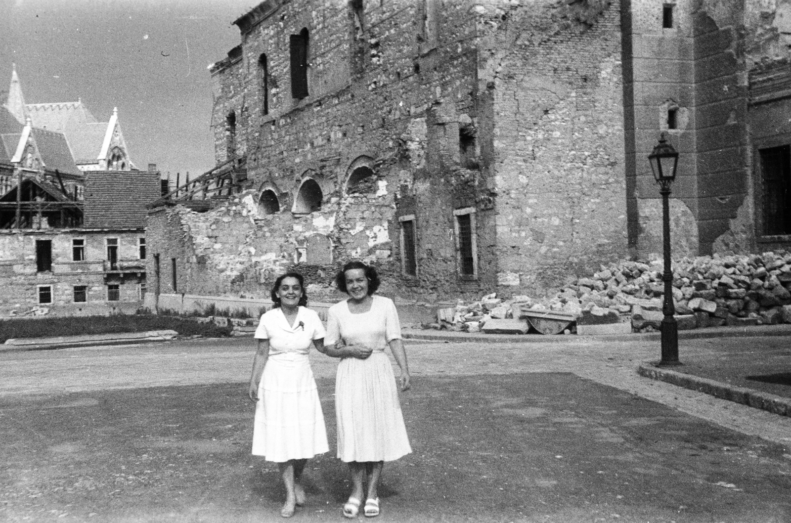 Hungary, Budapest I., Kapisztrán tér, jobbra a romos Mária Magdolna-templom. Háttérben balra a Magyar Országos Levéltár épülete., 1946, Bujdosó Géza, Budapest, damaged building, gas lamp, lady, smile, white dress, Fortepan #255596