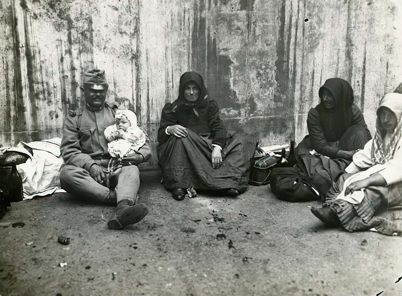 Hungary, Budapest VIII., Vas utca 9-11., a felvétel a laktanyává átalakított Felső Kereskedelmi Fiúiskola előtt készült, 1914. augusztusában. Vidékről bevonuló népfelkelő és hozzátartozói az I. világháború kitörése utáni mozgosítás idején., 1914, Országos Széchényi Könyvtár, Budapest, soldier, women, sitting on the ground, folk costume, hold in arms, kid, Fortepan #256121