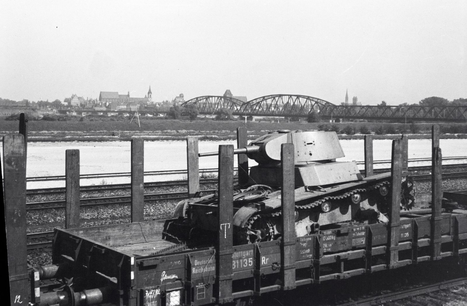 Poland, Toruń, rendező pályaudvar, a tehervagonon egy T–26 típusú szovjet könnyű harckocsi roncsa. Háttérben a Visztula folyó feletti Józef Piłsudski híd (Most im. marsz. Józefa Piłsudskiego). A híd takarásában a Szent János-székesegyház látható., 1942, Reményi József, wreck, tank, Fortepan #257774