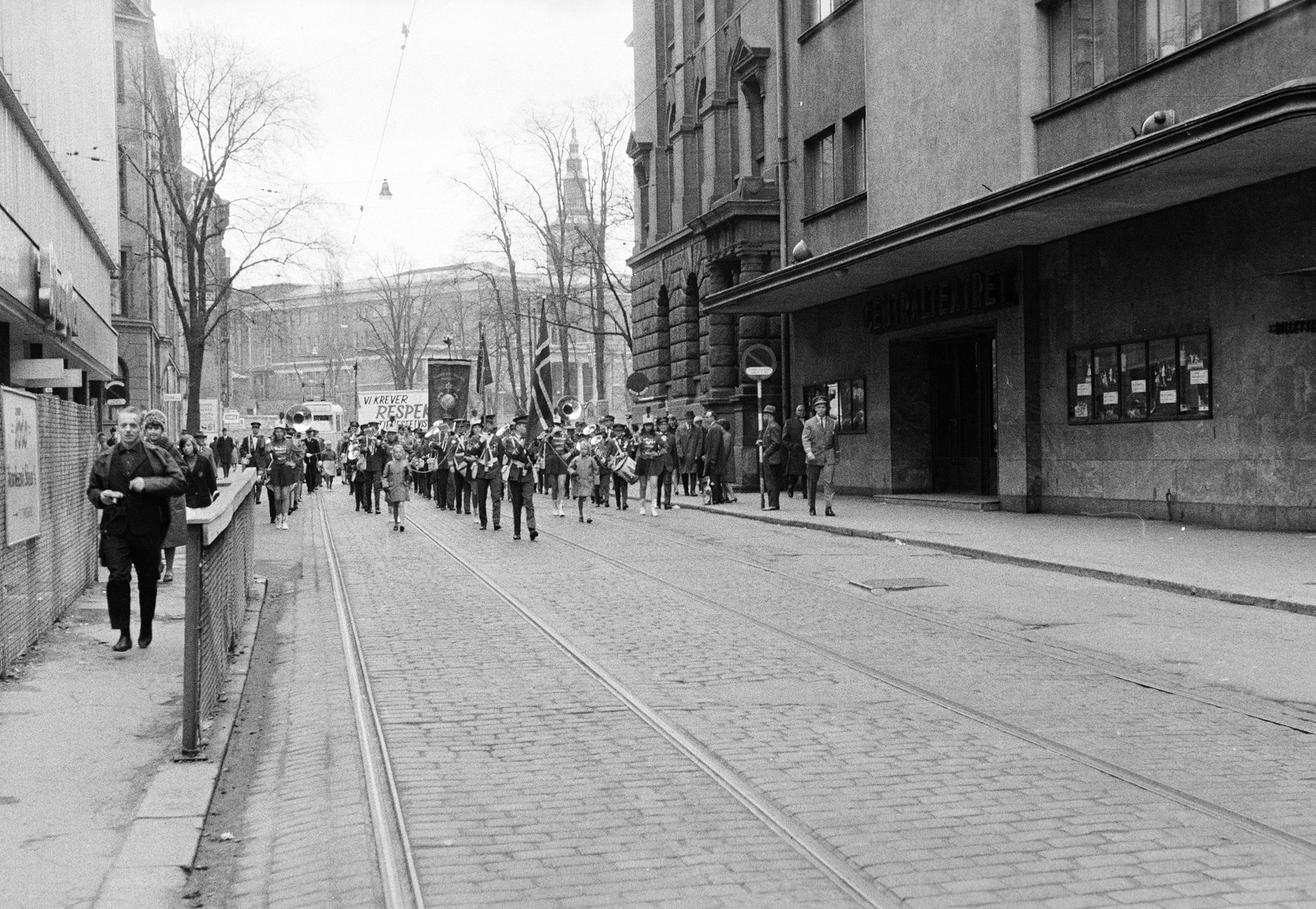 Norway, Oslo, Akersgata, felvonulók az Apotekergata - Grensen közötti szakaszon. Jobbra, az előtetős épület, a Centralteatret. Távolban a Det gamle biblioteket (A régi könyvtár) épülete mögött Svenska Margaretakyrkan tornyát lehet látni., 1965, Reményi József, theater, flag, wind band, march, majorette, tram, drum major, Fortepan #258469