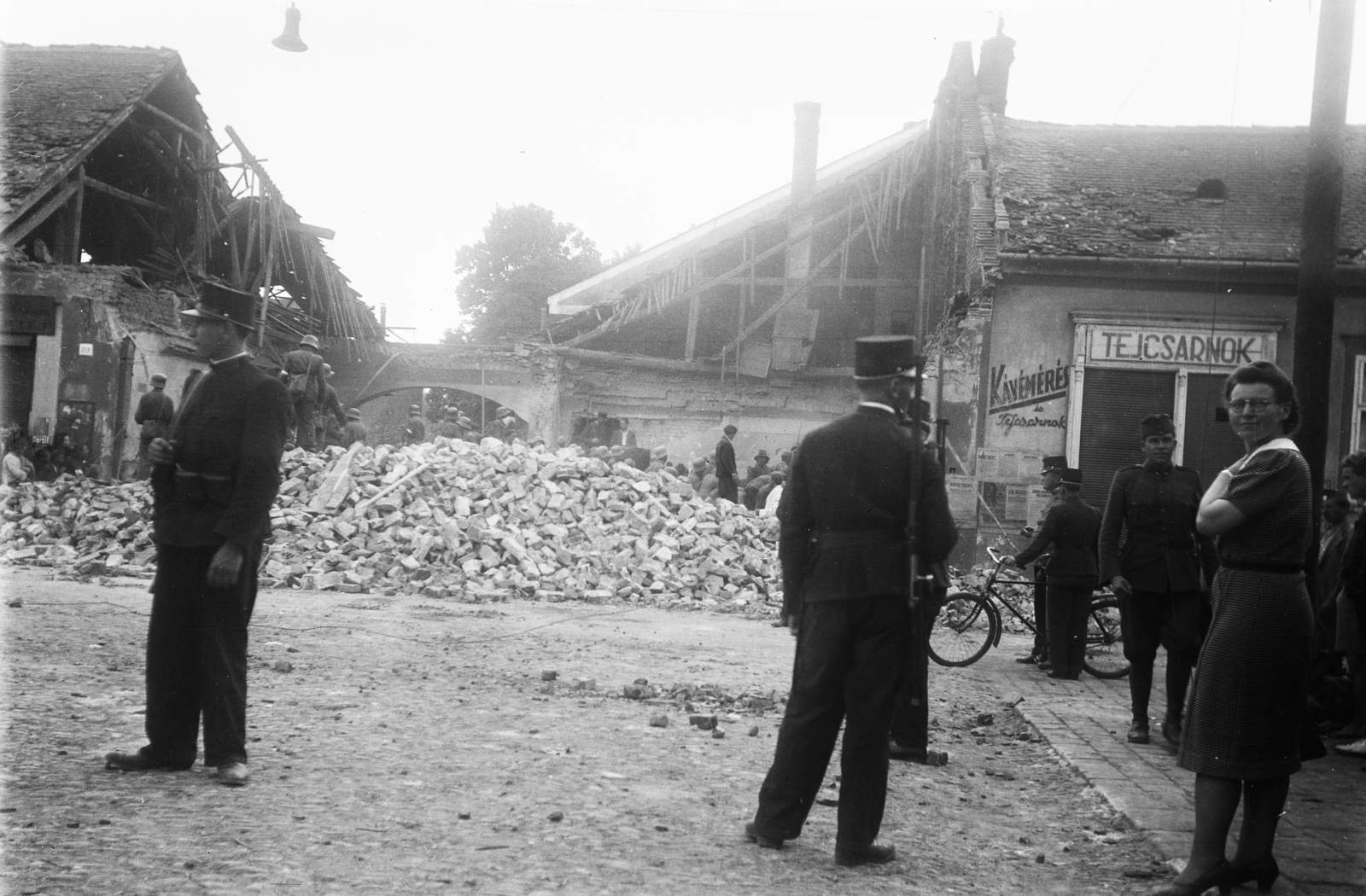 Szlovákia, Kassa, Bethlen Gábor körút (Kuzmányho ulica)-i házak az 1941. június 26.-i bombázás után. A romos ház helyén nyitották a Vojenská ulica-t., 1941, Reményi József, plakát, épületkár, kerékpár, magyar katona, rendőr, tűzfal, tejivó, kávémérés, kerékpáros rendőr, Fortepan #258814