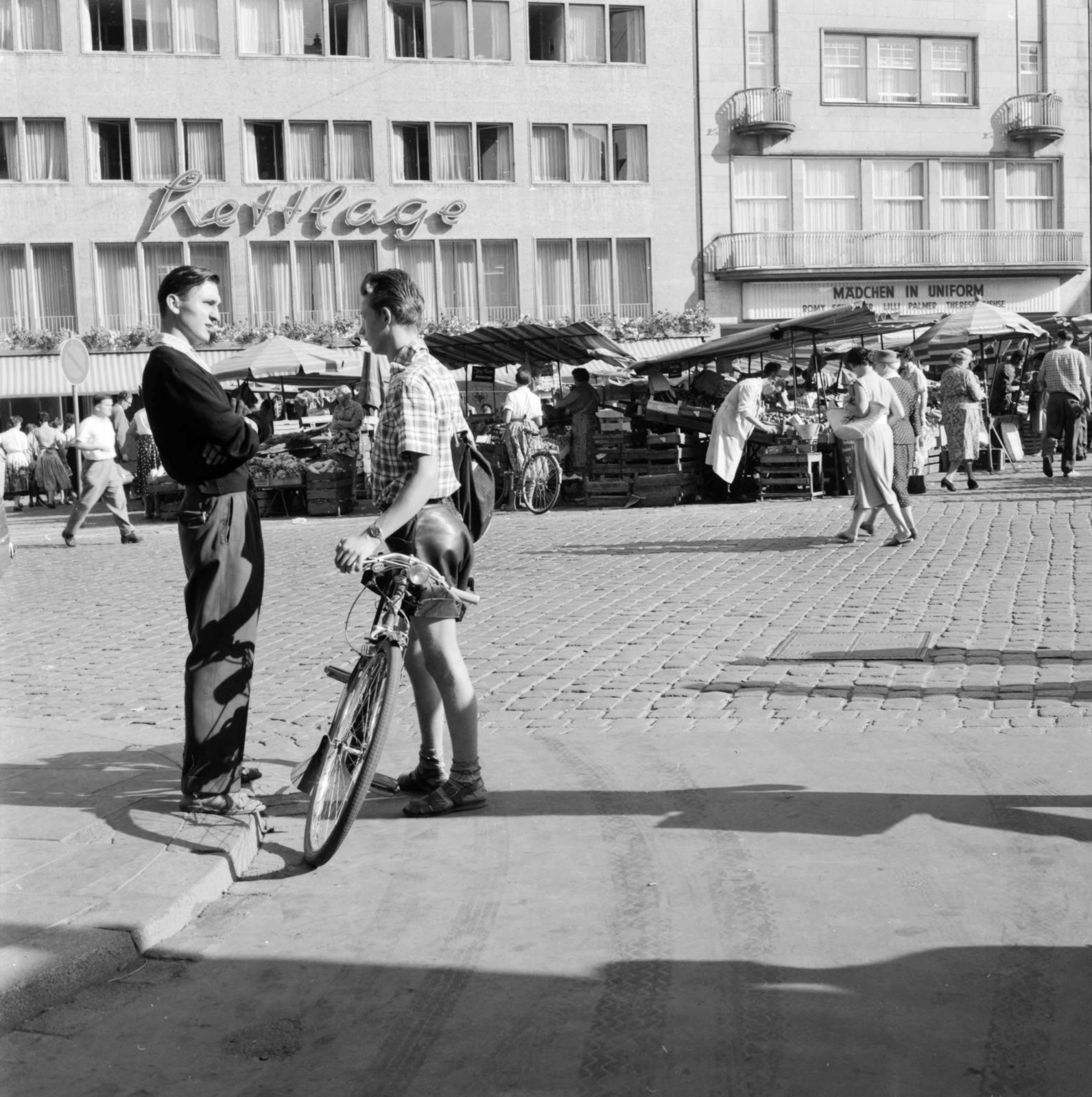 Germany, Bonn, Markt, Hettlage ruházati bolt, mellette a Metropol mozi., 1958, UWM Libraries, FRG, photo aspect ratio: square, wrist watch, talks, bicycle, leather pants, market, Fortepan #259356