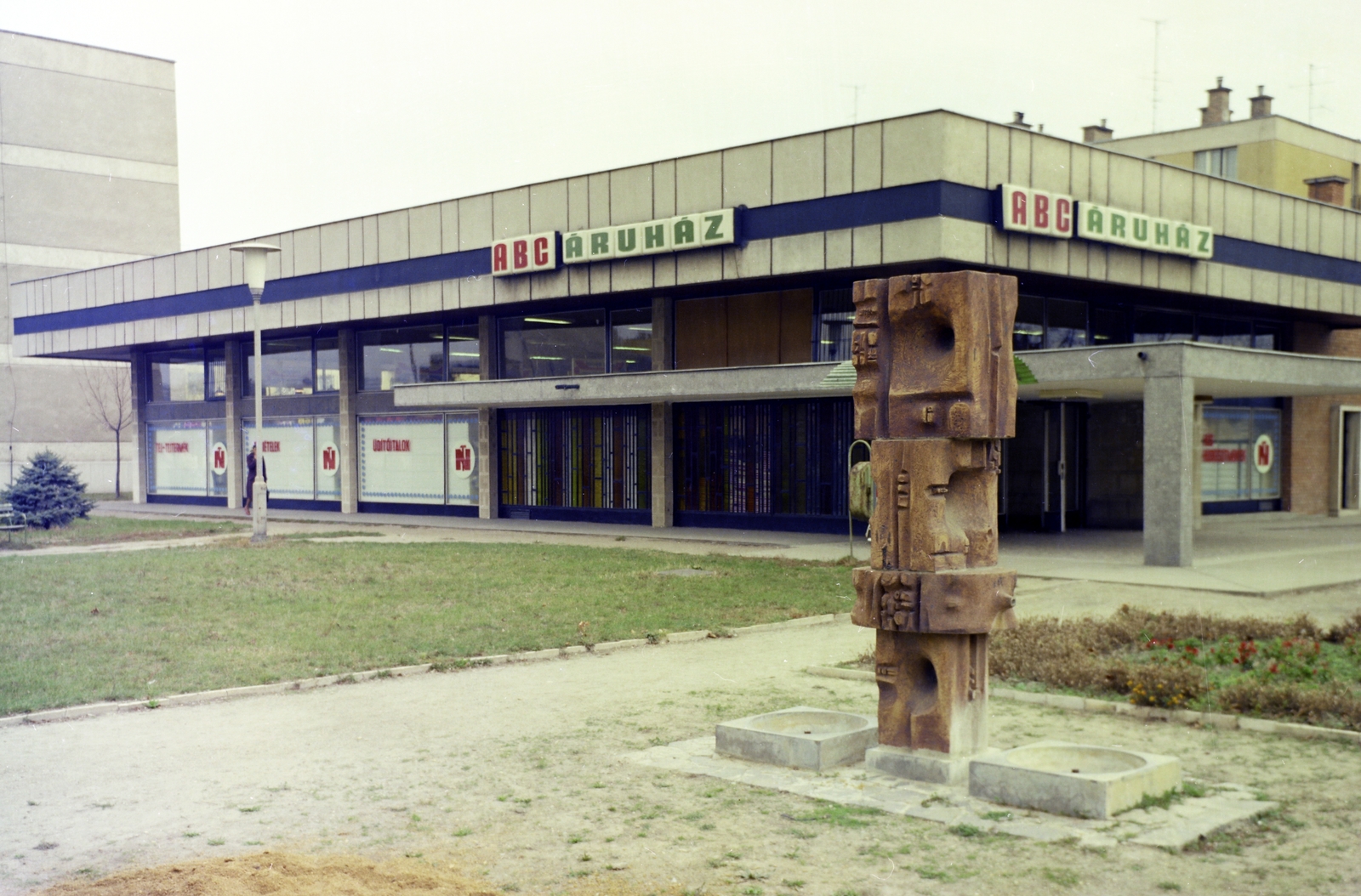 Magyarország, Szekszárd, Tartsay Vilmos lakótelep, ABC Áruház. Előtérben Pázmándi Antal 1970-ben felállított samott Figurális kút-ja., 1980, Faragó György, színes, Fortepan #261424