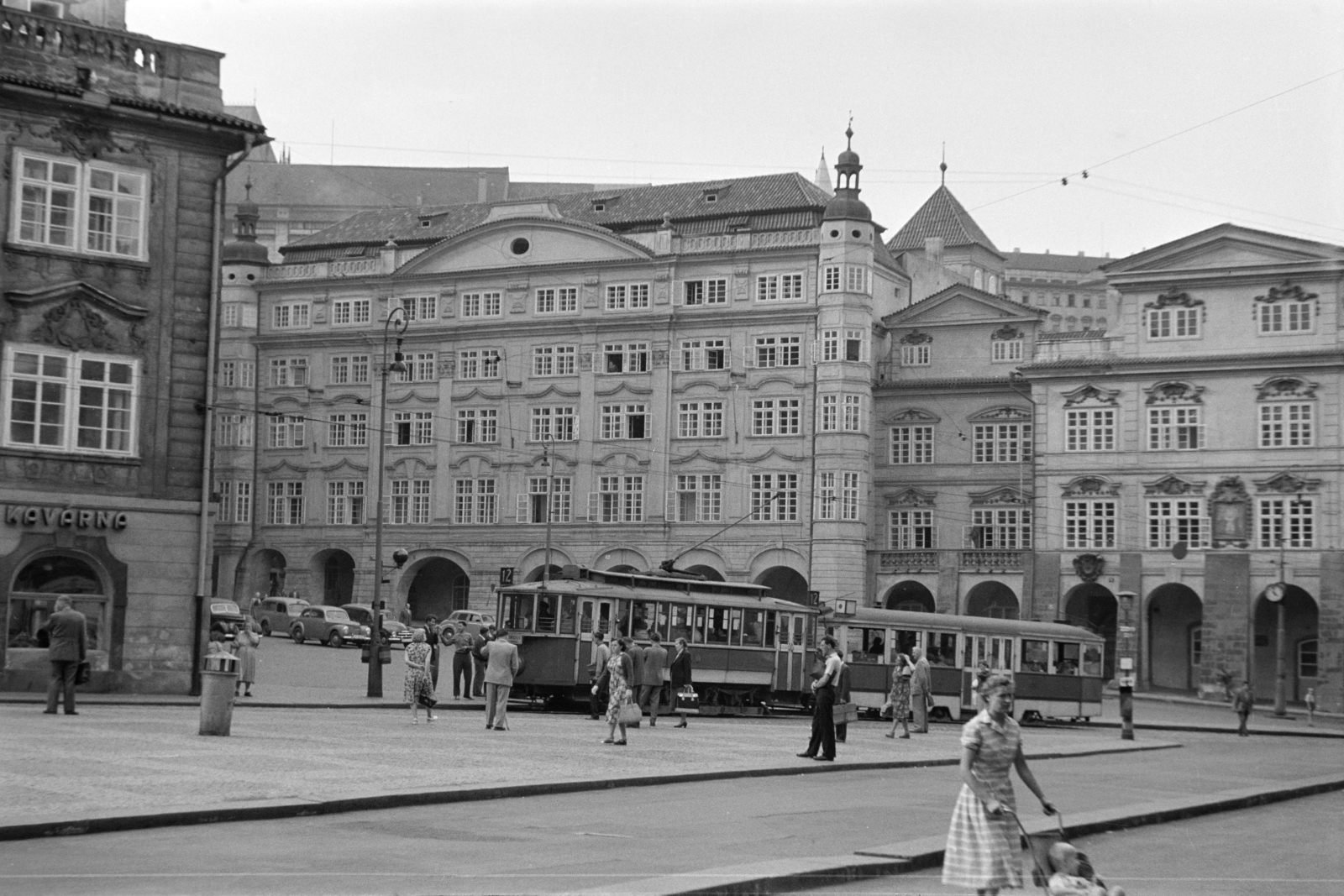 Czech Republik, Prague, Kisoldal tér (Malostranské námesti). Szemben középen a Palác Smiřických., 1956, Faragó György, public clock, public transport line number, tram, trash can, pantograph, Czechoslovakia, Fortepan #261635