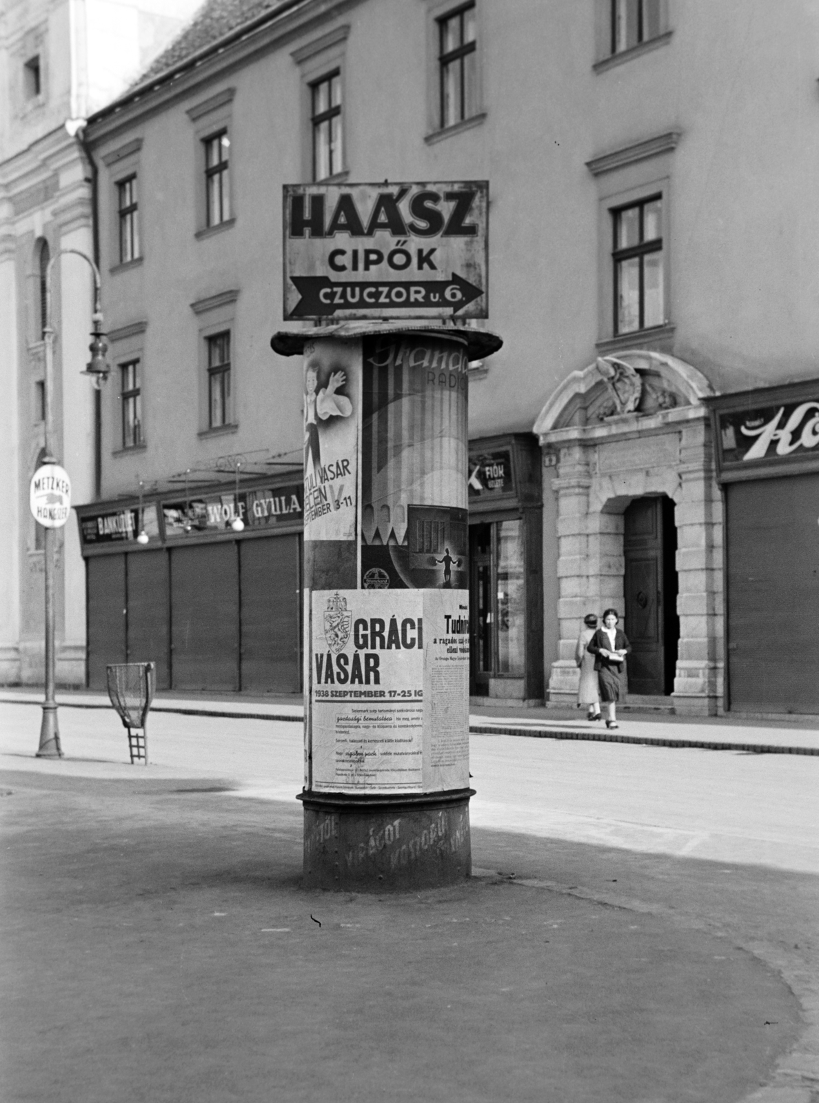 Hungary, Győr, Széchenyi tér, hátterében a Loyolai Szent Ignác bencés templom és a rendház., 1938, Nagy István, poster, ad pillar, trash can, shoe store, Fortepan #264251