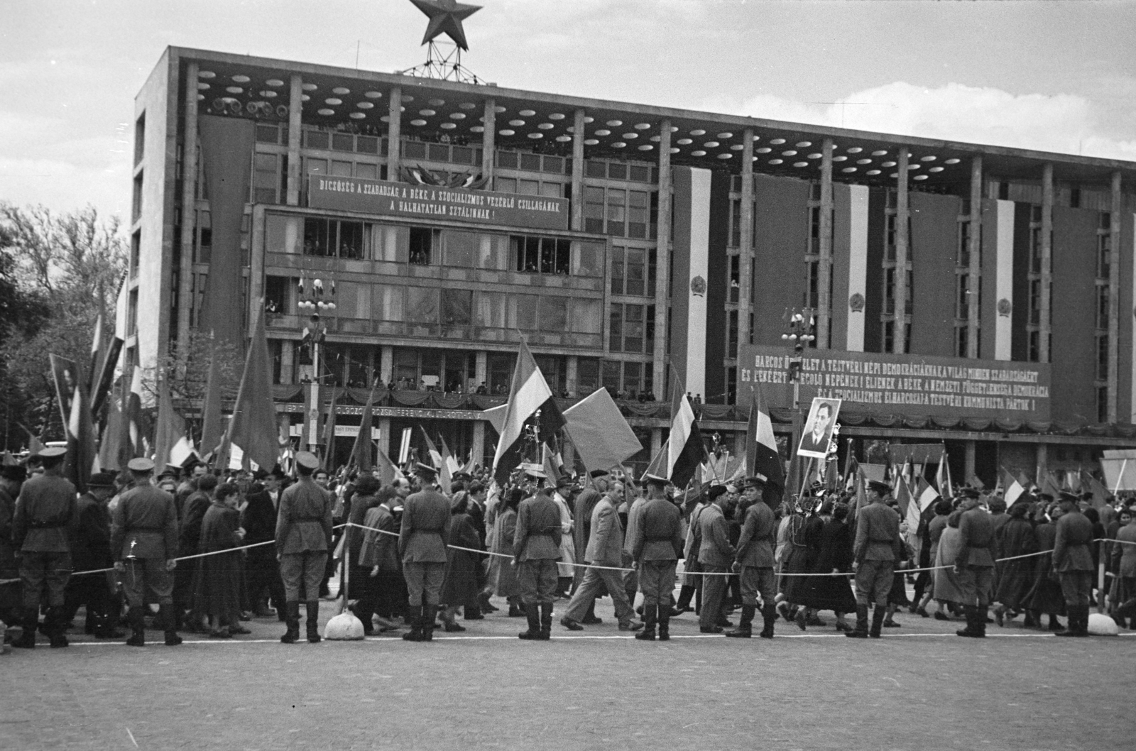 Hungary, Budapest XIV.,Budapest VI., Ötvenhatosok tere (Felvonulási tér), háttérben a Dózsa György úton a MÉMOSZ (Magyarországi Építőipari Munkások Országos Szövetsége) székháza. Május 1-i felvonulás., 1953, Horváth József, MÉMOSZ-organisation, label, Red Star, march, 1st of May parade, bunting, Budapest, Fortepan #264909