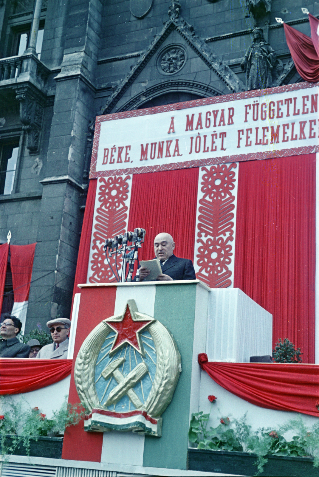 Hungary, Budapest V., Kossuth Lajos tér, választási nagygyűlés. A Parlament főbejárata előtti szónoki emelvényen Rákosi Mátyás. Balra sötét szemüvegben Gerő Ernő, mellette Erdei Ferenc., 1953, Horváth József, winners' podium, Rákosi crest, speech, colorful, political decoration, drapery, Budapest, Fortepan #265637