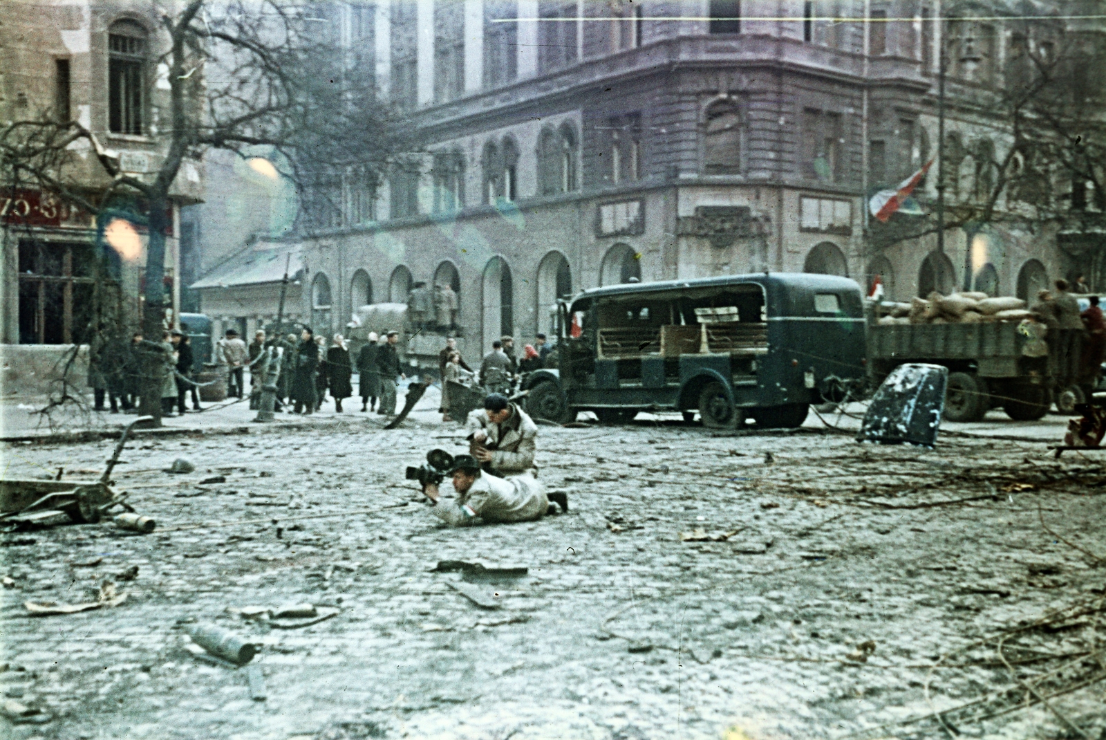 Hungary, Budapest IX., Ferenc körút, operatőr munkában a Tompa utca torkolatánál. Háttérben egy Csepel D-350 rendőrségi riadókocsi roncsa., 1956, Horváth József, Best of, movie camera, wreck, colorful, hat, revolution, Csepel-brand, Budapest, Fortepan #265790