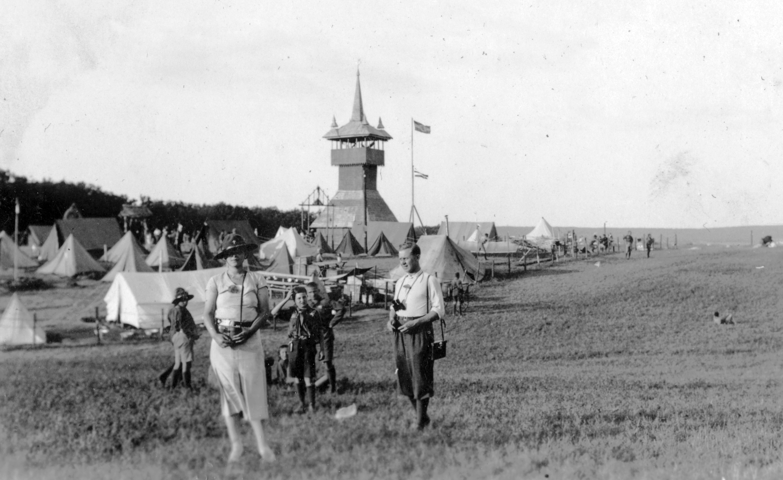Hungary, Gödöllő, 4. Nemzetközi Cserkész Világtalálkozó (Jamboree), Nyírbátori harangláb., 1933, Fortepan, flag, tableau, field, tent, kids, telescope, man, fence, woman, scouting, camp, tower, camping site, yoke, ornamental gates, Fortepan #26711