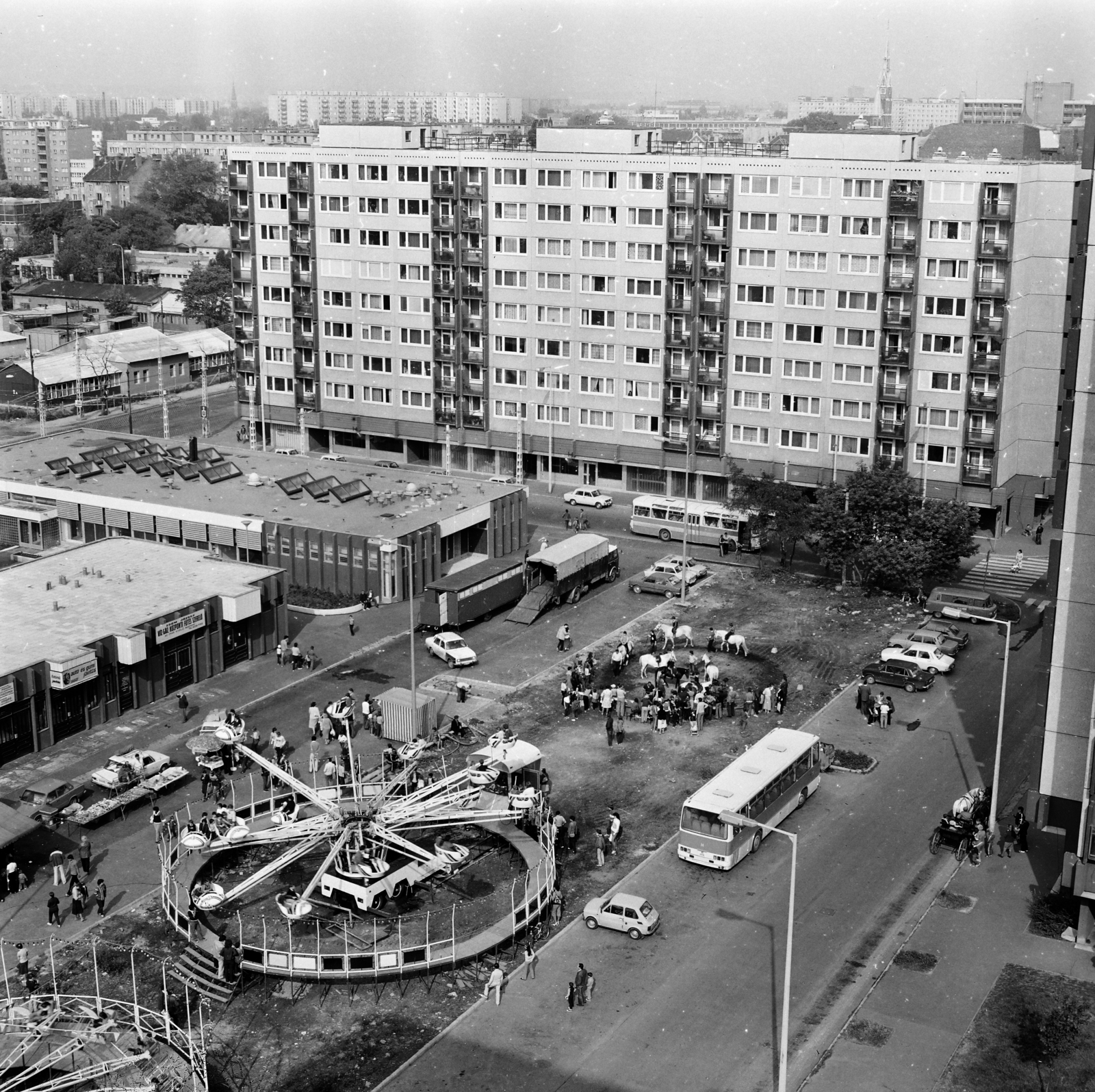 Magyarország, Budapest XIII., kilátás a Kárpát utca 37-es számú házból a Tisza (Tisza Antal) utca melletti vurstlira. Szemben a Pannónia (Rajk László) utca melletti panelház, ettől balra a Dráva utca látható., 1983, Glósz András, autóbusz, panelház, lakótelep, körhinta, Ikarus-márka, vurstli, Budapest, Fortepan #268545