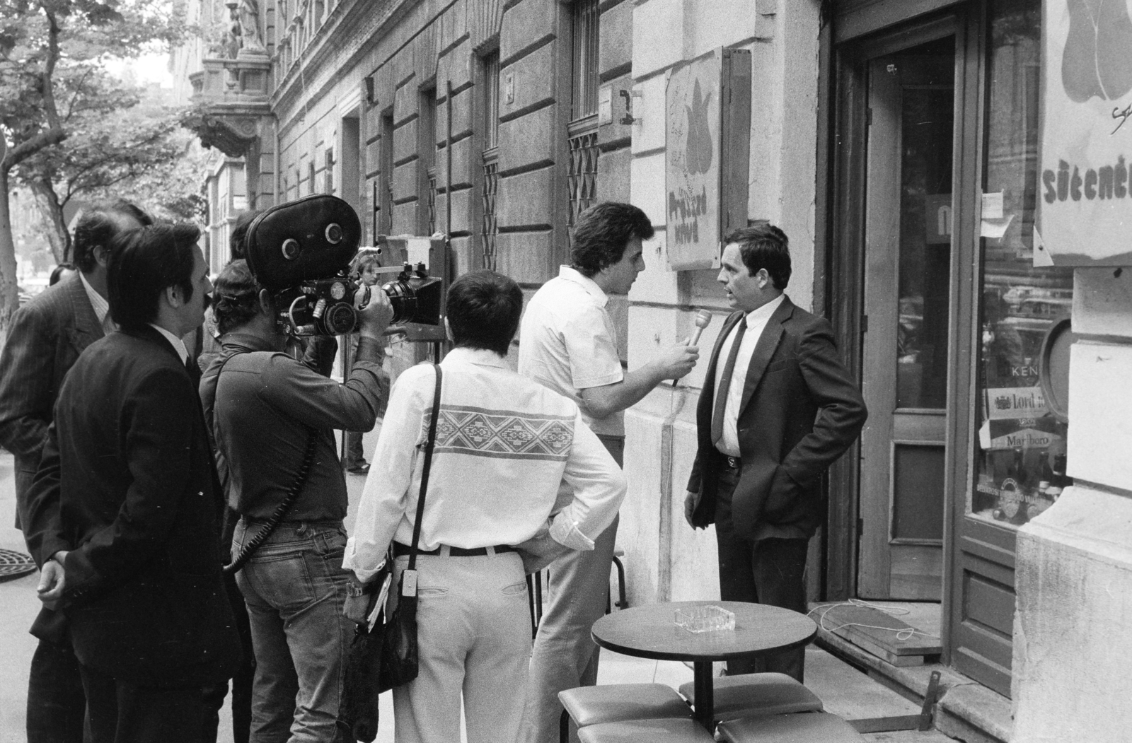 Magyarország, Budapest V., Nádor utca (Münnich Ferenc utca) a felvétel a 34. számú ház előtt készült. Sütő Péter újságíró, műsorvezető, rendező, szerkesztő riportot készít az MTV Reflektor Magazinjának., 1983, Kanyó Béla, riporter, filmforgatás, filmkamera, Budapest, üzletportál, interjú, cukrászda, Fortepan #268714