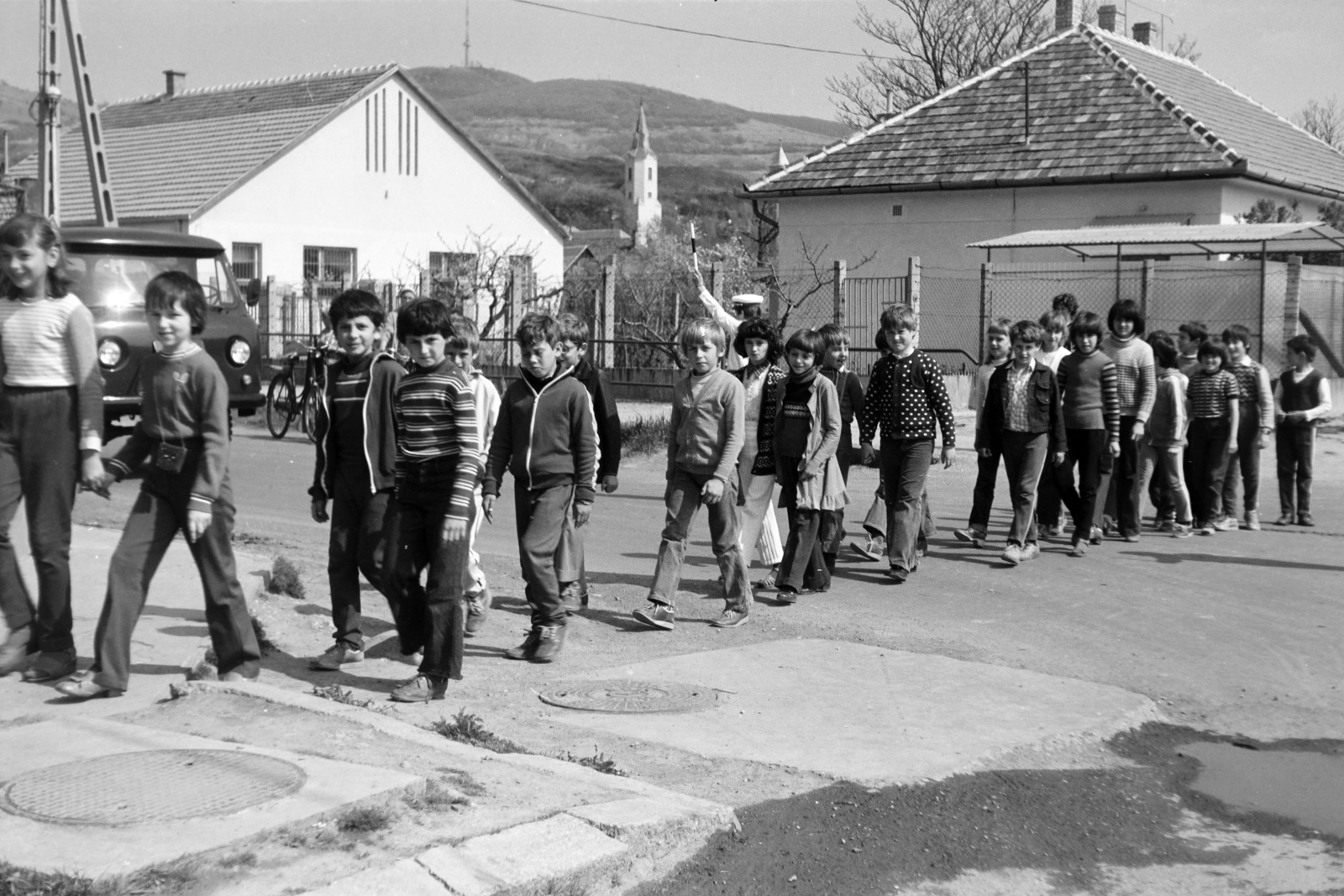 Magyarország, Tarcal, az Árpád utca a Munkácsy utca kereszteződésénél, a felvétel az általános iskolánál készült. Háttérben az Urunk Mennybemenetele-templom, ettől jobbra a háztető sarkánál a református templom toronycsúcsa látszik., 1982, Leskó Imre, gyerekek, menet, Fortepan #269832