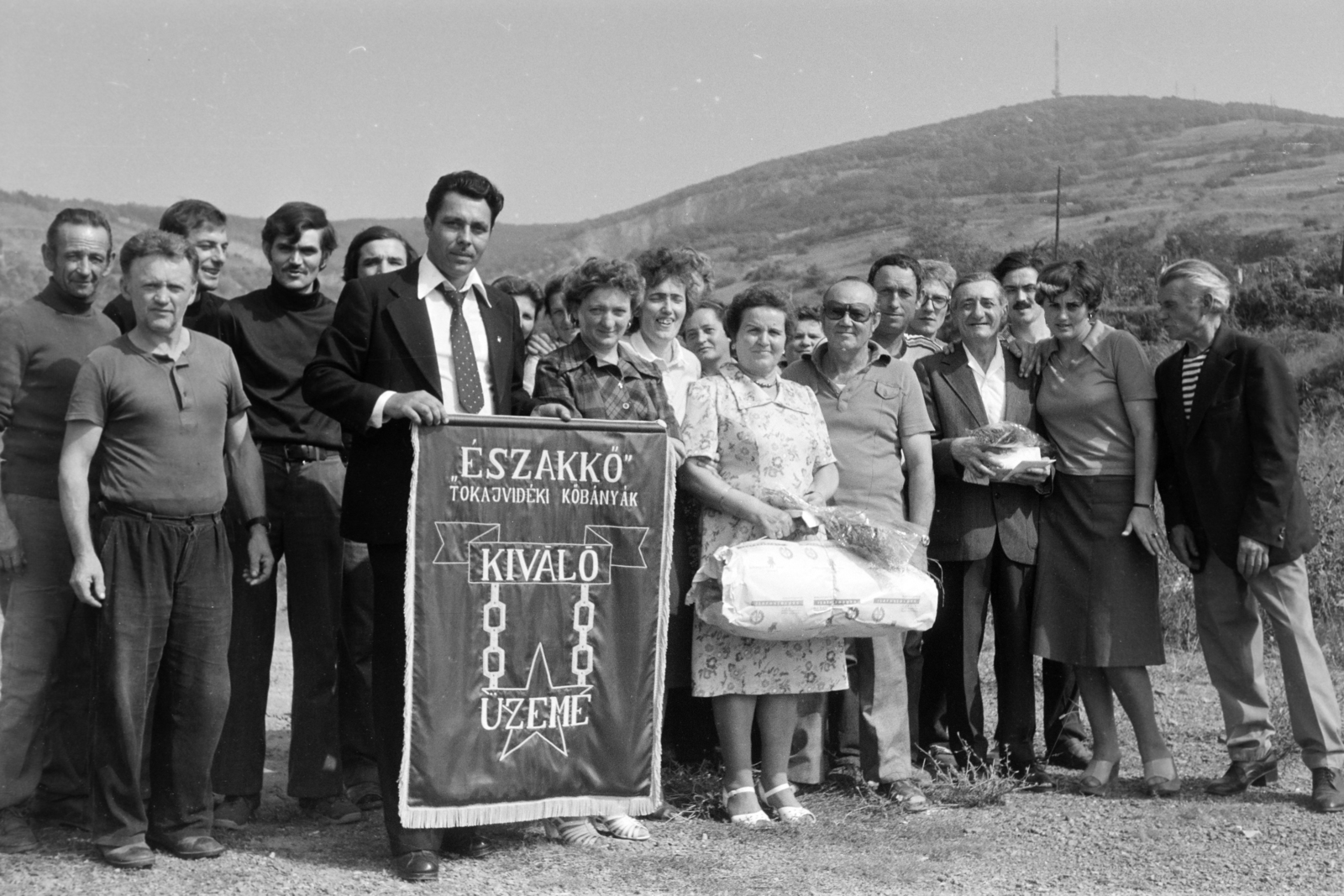 Hungary, Tarcal, a Tokajvidéki Kőbányák Északkő Üzemének dolgozó, a Kiváló Üzem díj zászlójával. Háttérben a Kopasz-hegy és a TV adótorony., 1981, Leskó Imre, tableau, pride, Excellent Company Award, Fortepan #269909