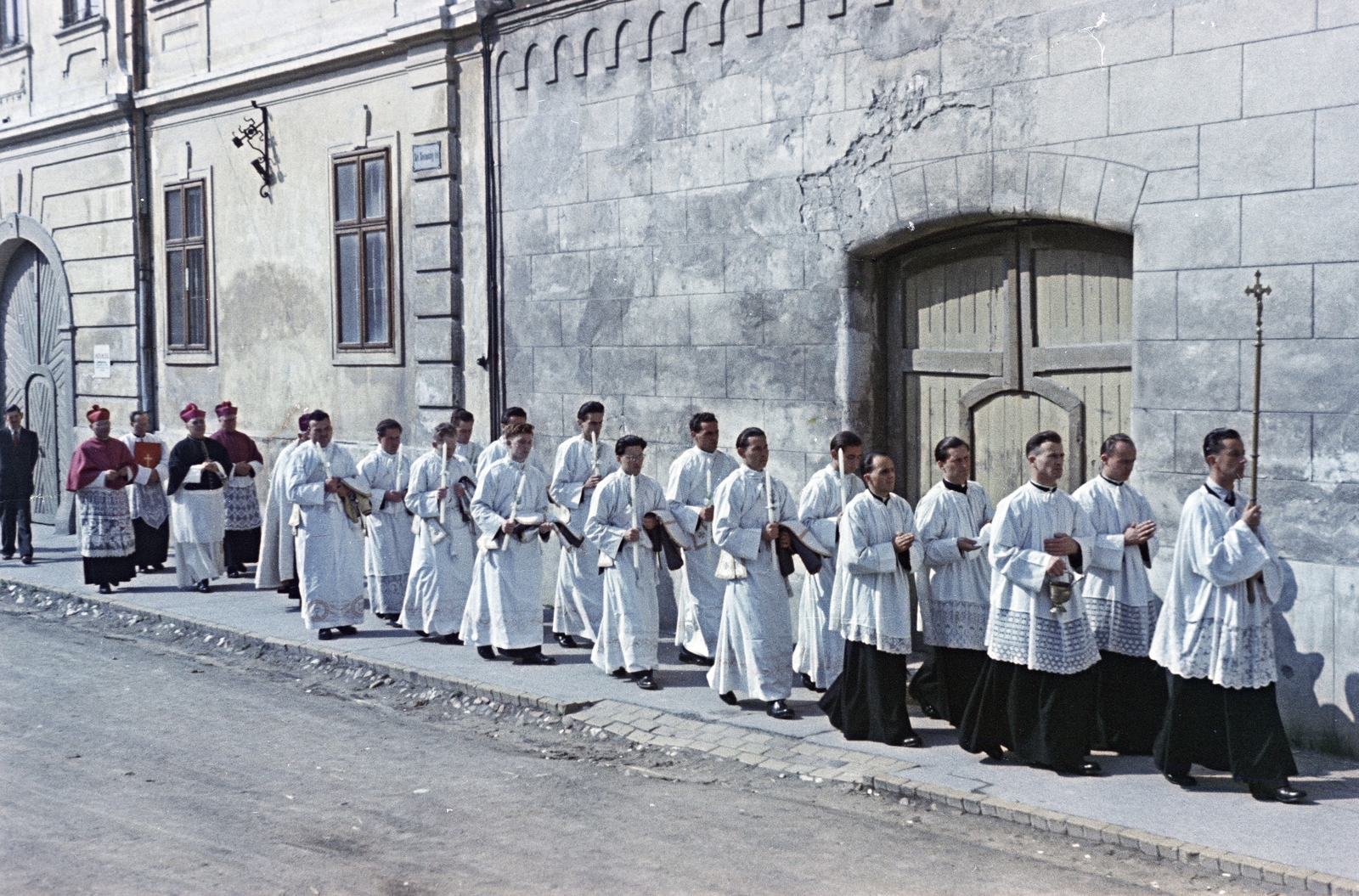 Hungary, Veszprém, Vár (Tolbuhin) utca, a felvétel a Szent István ferences templom udvarának kapuja előtt készült. Gyertyával a kezükben haladnak a végzett teológusok a papszentelés helyszínére, a Szent Mihály-székesegyház felé. Hátrébb Bíró-Giczey ház előtt, sötét pelerinnel a válán Badalik Bertalan veszprémi püskök látható., 1956, Hámori Gyula, march, priest, colorful, candle, surplice, Fortepan #276208