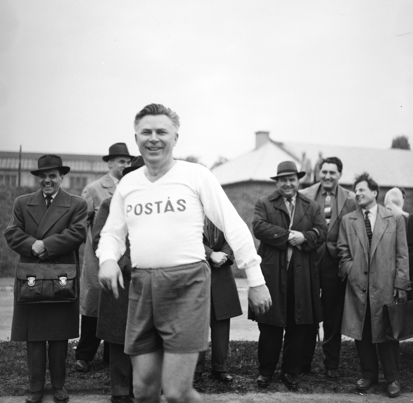 Magyarország, Budapest XIV., Egressy úti Postás SE sporttelep, háttérben a Báróczy utca túloldalán a Posta Központi Járműtelep épületei. Előtérbrn Besenyei Miklós a Postások Szakszervezetének főtitkára., 1960, Németh Tamás, Budapest, sport mez, nevetés, aktatáska, Fortepan #276968