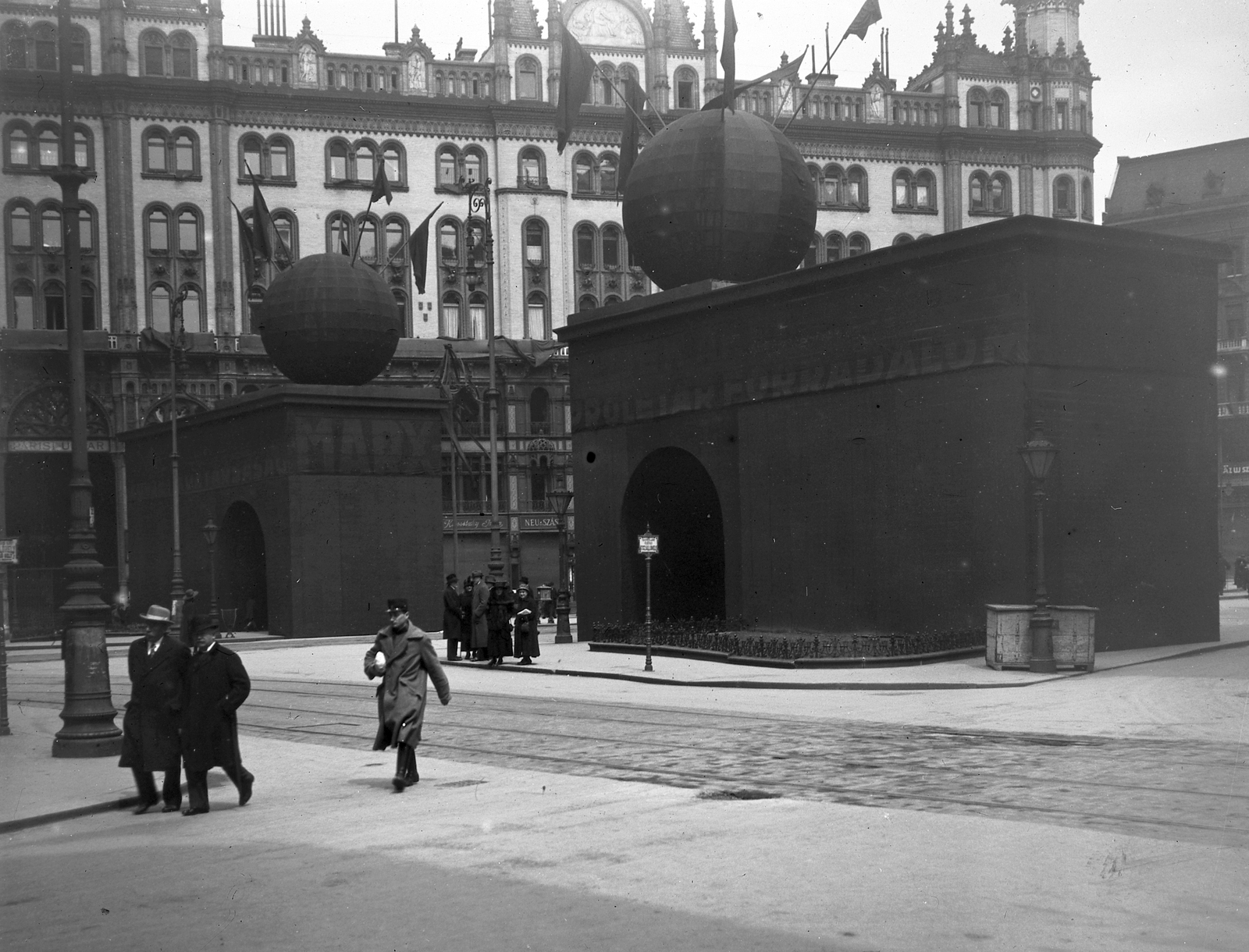 Magyarország, Budapest V., Ferenciek tere, Pázmány Péter és Werbőczy István szobra május 1-i dekorációval eltakarva, háttérben a Párizsi udvar., 1919, Schoch Frigyes, zászló, járókelő, utcakép, politikai dekoráció, május 1, lámpaoszlop, középület, Tanácsköztársaság, tábla, eklektikus építészet, Budapest, Henrik Schmahl-terv, Fortepan #27908