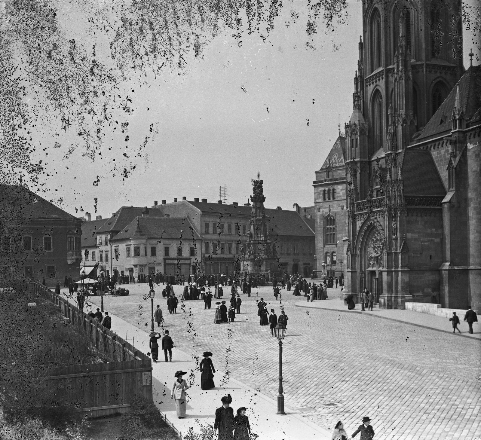 Magyarország, budai Vár, Budapest I., Szentháromság tér, jobbra a Mátyás-templom., 1906, Kurutz Márton, kalap, templom, emlékmű, utcakép, életkép, léckerítés, elegancia, kockakő, szentháromság szobor, Budapest, Fortepan #27950