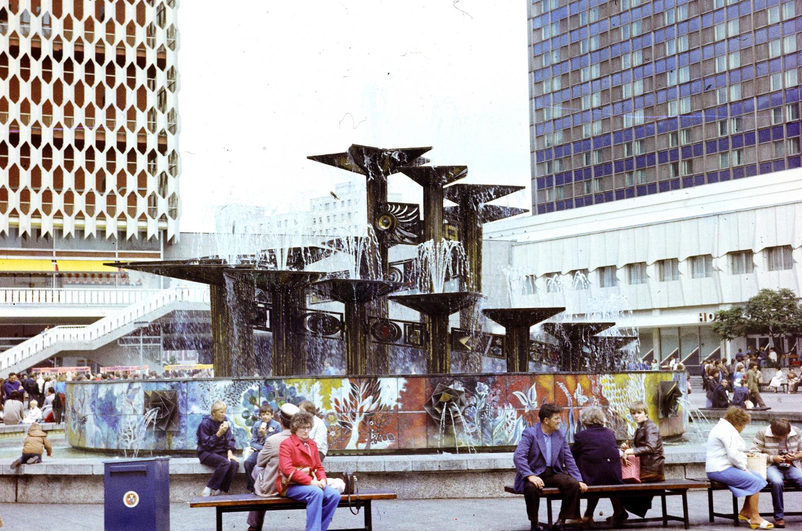 Németország, Berlin, Kelet-Berlin, Alexanderplatz. Előtérben a Népek Barátsága szökőkút (Brunnen der Völkerfreundschaft), mögötte háttérben balra a Centrum Áruház, jobbra a Hotel Stadt Berlin., 1974, Domokos József, NDK, Kelet-Berlin, színes, Fortepan #284486