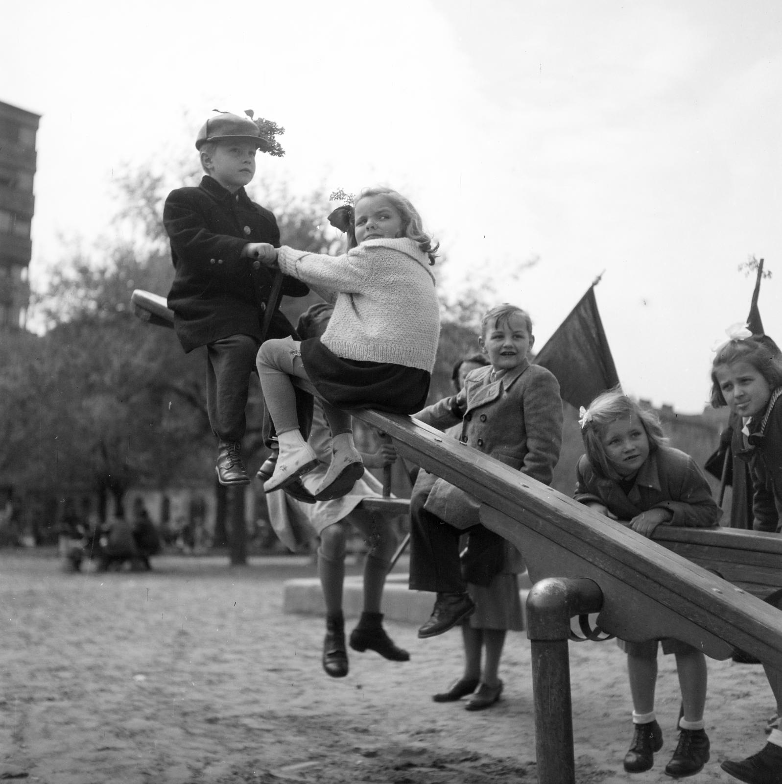 Magyarország, Budapest VIII., II. János Pál pápa (Köztársaság) tér, háttérben balra az Országos Társadalombiztosító Intézet (OTI) lakóház-csoport 14. szám alatti épületének a sarka a Vay Ádám utcánál., 1955, Gara család, Budapest, libikóka, gyerekek, játszótér, visszanézés, Fortepan #285850