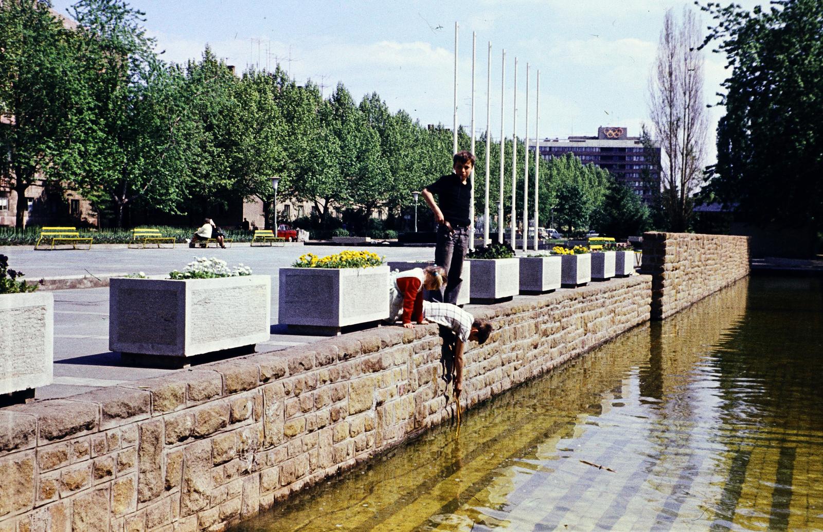 Magyarország, Dunaújváros, park a Vasmű út mellett, a felvétel a Kodály Zoltán utca felől az Eszperantó út felé készült, ahol a Garzonház látszik. Balra a házak földszintjén a Gagarin térre vezető átjárók vannak., 1973, Kozák, színes, Fortepan #286734