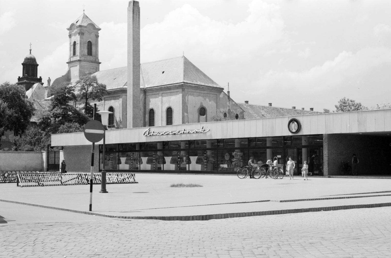 Hungary, Kecskemét, Horváth Cirill tér, Piaccsarnok, háttérben a Szentháromság piarista templom és a Piarista Gimnázium tornya., 1966, Építésügyi Dokumentációs és Információs Központ, VÁTI, bicycle, church, shop, store, road sign, bicycle holder, Piarist Order, neon sign, Fortepan #28991