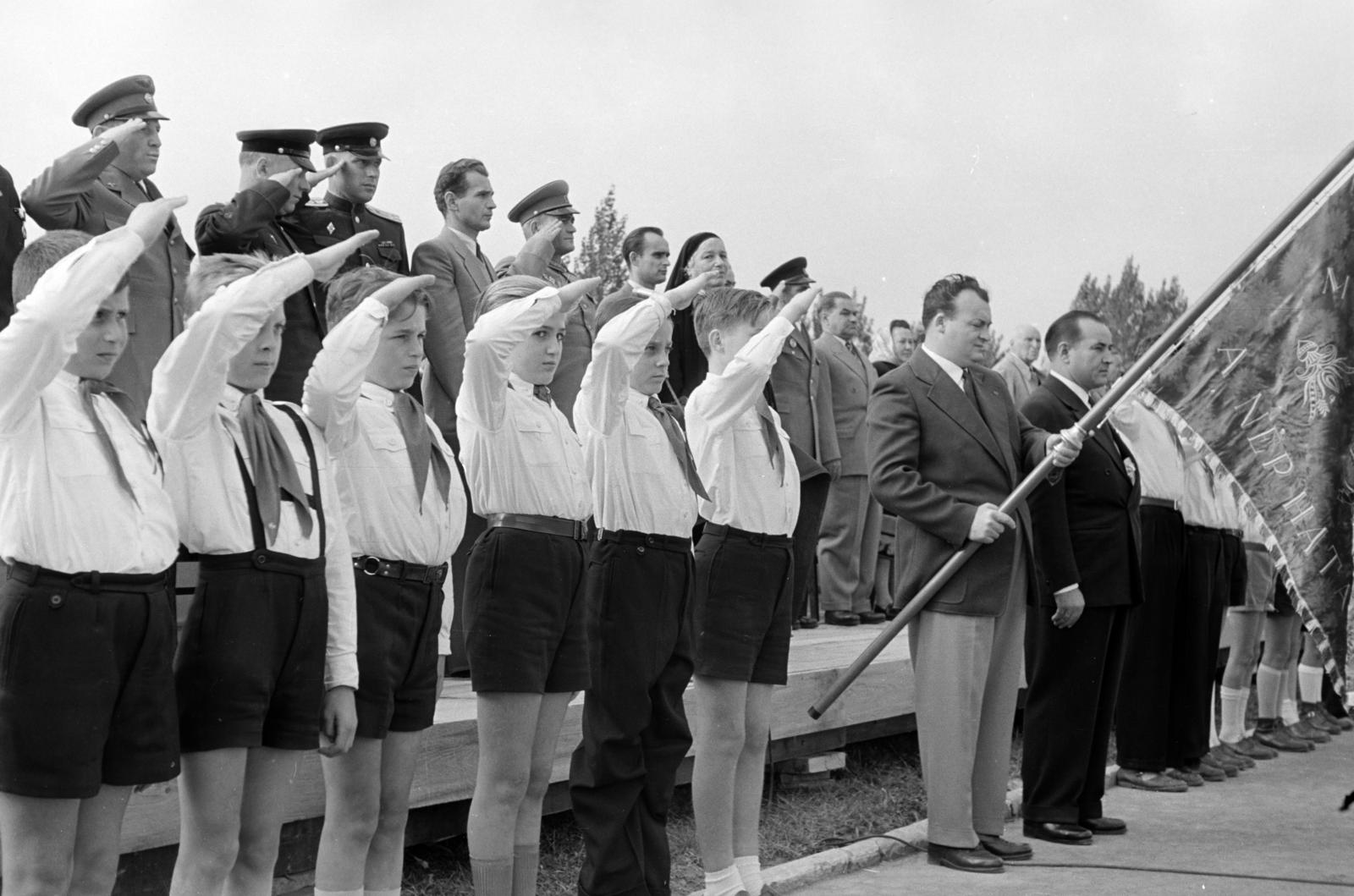 Magyarország, Budapest XII., Csörsz utca, a Magyar Testnevelési Főiskola sporttelepe. A felvétel 1957. március 9-én, a XII. kerületi Ságvári Endre munkásőrzászlóalj megalakulásakor, a névadó és a Magyar Optikai Művek (MOM) dolgozói által adományozott csapatzászló átadási ünnepségén készült. A csapatzászlóval Gyarmati László a MOM párttitkára és mellette Posch Gyula, a MOM igazgatója, mögöttük félig takarva Ságvári Endre édesanyja, aki az első szalagot kötötte fel a zászlórúdra., 1957, Hegyvidéki Helytörténeti Gyűjtemény, Budapest, Fortepan #290182