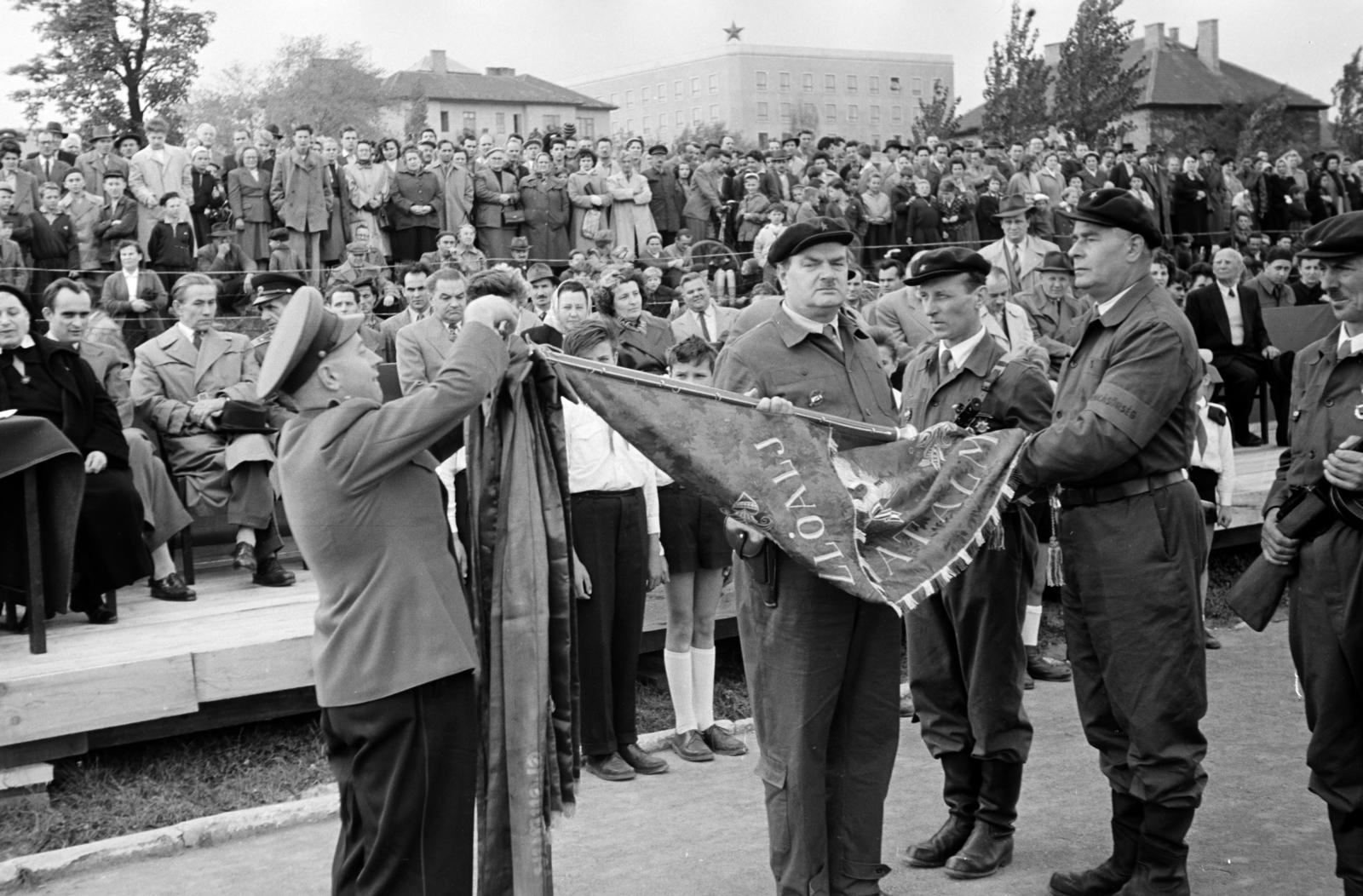 Magyarország, Budapest XII., Csörsz utca, a Magyar Testnevelési Főiskola sporttelepe. A felvétel 1957. március 9-én, a XII. kerületi Ságvári Endre munkásőrzászlóalj megalakulásakor, a névadó és a Magyar Optikai Művek (MOM) dolgozói által adományozott csapatzászló átadási ünnepségén készült. Háttérben középen a Magyar Optikai Művek (MOM) irodaépülete., 1957, Hegyvidéki Helytörténeti Gyűjtemény, Budapest, Fortepan #290189