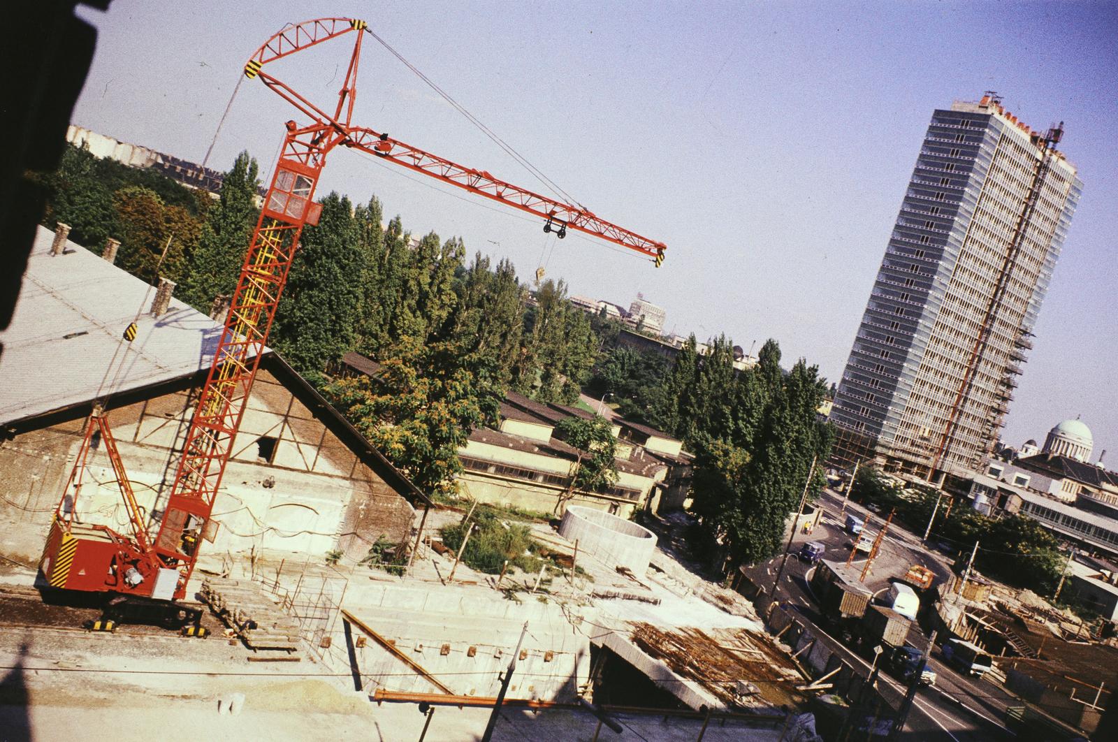Magyarország, Budapest IX.,Budapest VIII., Nagyvárad tér, előtérben az aluljáró és a metró építési területe. Mögötte balra az Orczy kert (Asztalos János Ifjúsági Park), ettől jobbra az Orczy (Mező Imre) út és a SOTE (később Semmelweis Egyetem) Elméleti Tömbjének építkezése. A kép jobb szélén a Magyarok Nagyasszonya (Rezső) téri templom látszik., 1975, Szomolányi József, építkezés, felhőkarcoló, színes, daru, Budapest, Fortepan #302838
