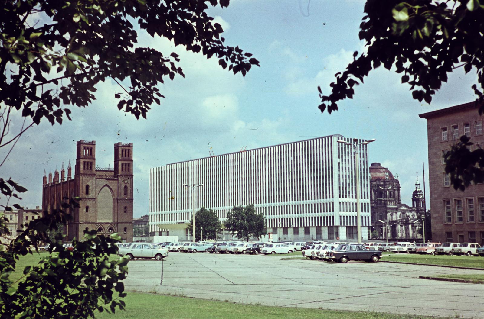 Németország, Berlin, Kelet-Berlin, a Kurstraße-Werderscher Markt sarok az Oberwallstraße felöl nézve. A kép bal szélén a Friedrichwerdersche Kirche, középen a Ministerium für Auswärtige Angelegenheiten der DDR (az NDK Külügyminisztériuma) mára elbontott épülete, a háttérben a Berliner Dom épülete., 1964, Szomolányi József, modern építészet, parkoló, színes, gótika, Fortepan #302888