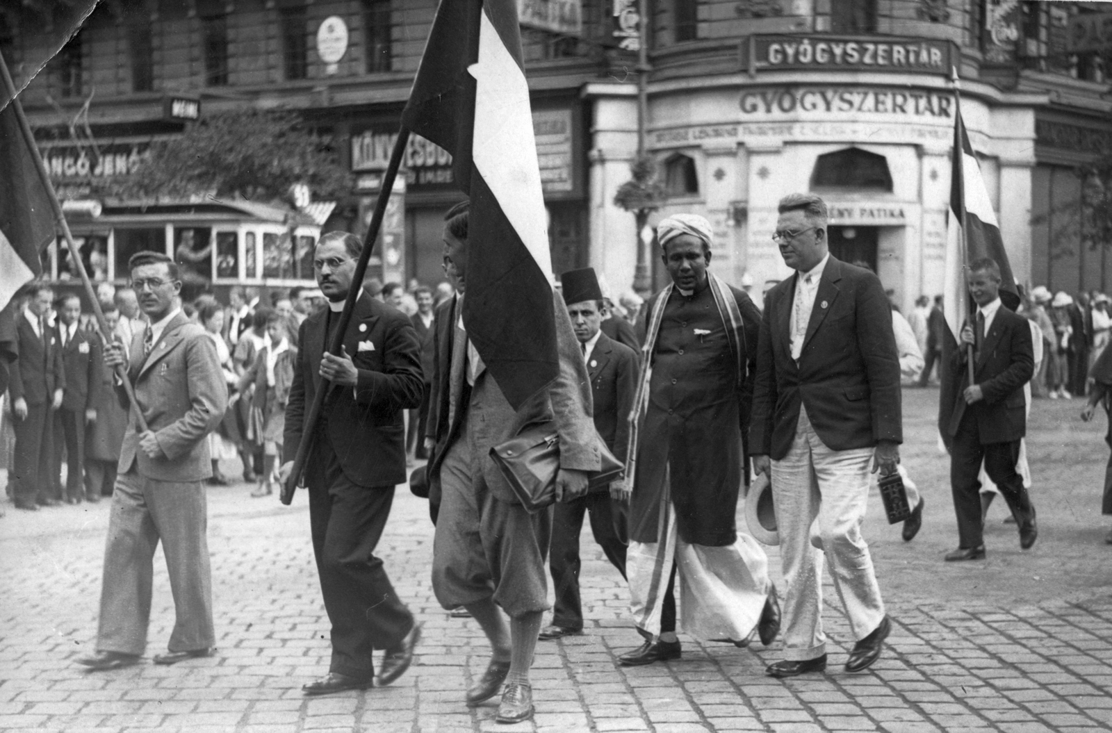 Magyarország, Budapest VIII., Rákóczi út - József körút sarok az Erzsébet körút felől nézve. A 9. Keresztyén Világkonferencia résztvevői., 1935, Makkai Sándor Protestáns Népfőiskolai Egyesület gyűjteménye, zászló, könyvesbolt, villamos, felvonulás, gyógyszertár, bricsesz, turbán, fez, Örkény Patika, Budapest, Fortepan #30366