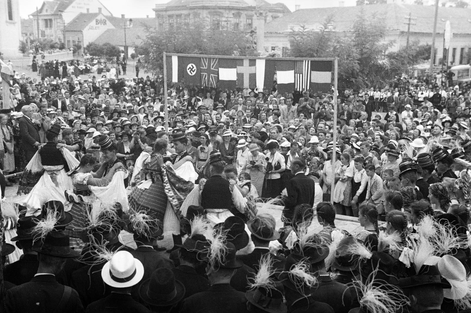 Hungary, Mezőkövesd, Szent László tér, balra a Szent László-templom, háttérben a Szűz Mária - Szentek szoborcsoport és a Mátyás király út házsora., 1937, Inkey Tibor, mass, dance, flag, folk costume, swastica, maidenhair, Fortepan #304753